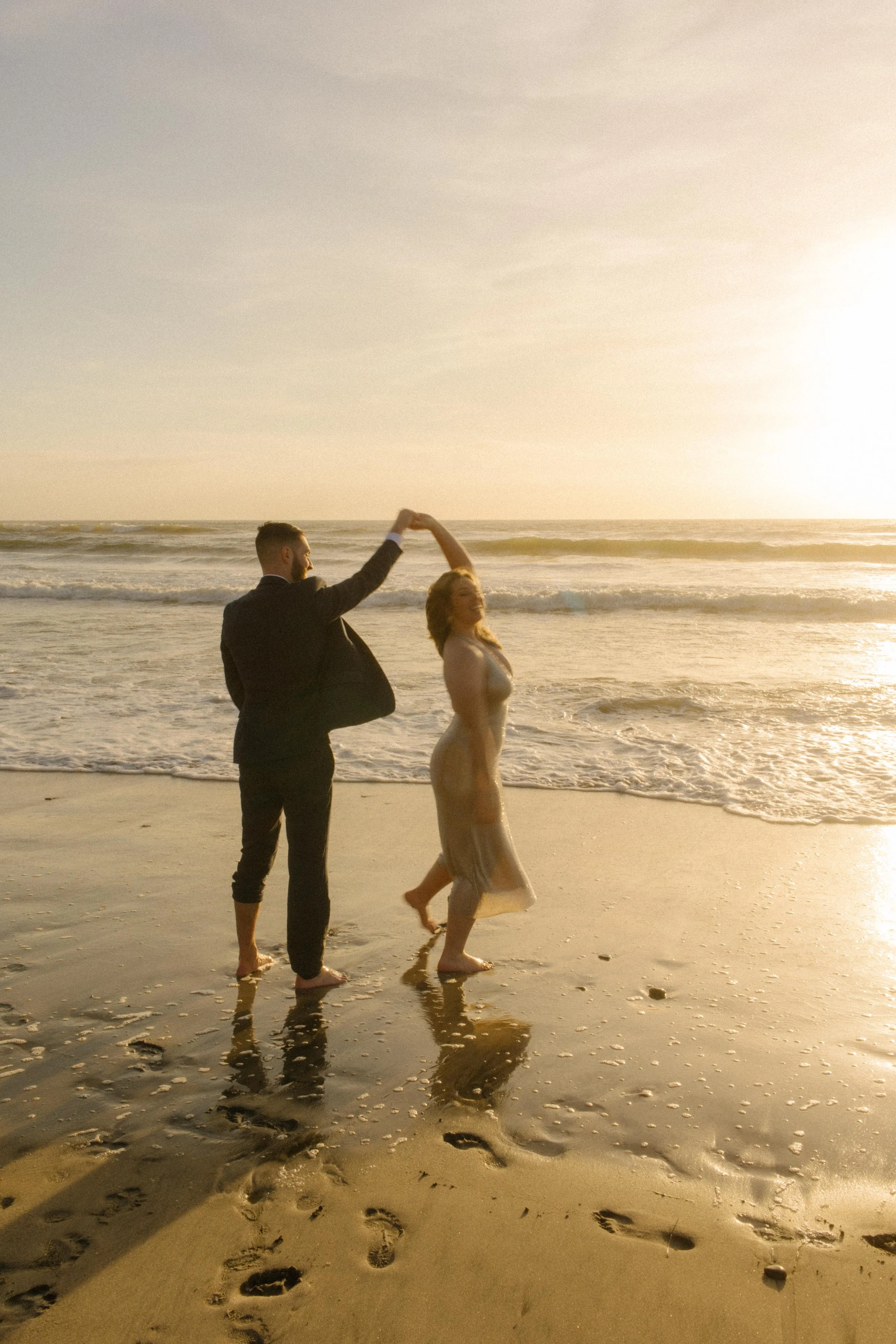 A barefoot couple dances in the waves during sunset, creating cinematic San Diego engagement photos full of movement and light.