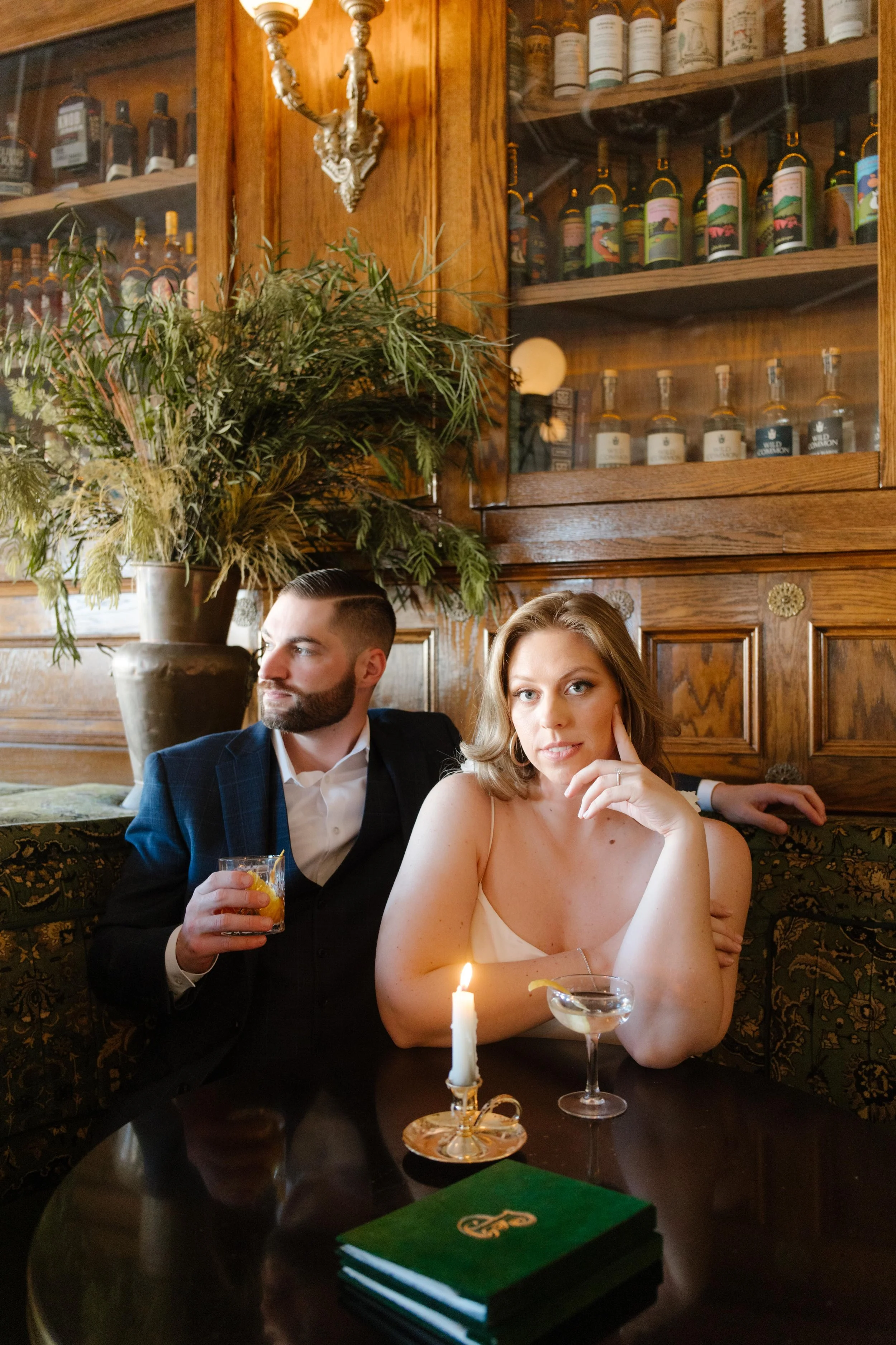 The couple poses confidently at a candlelit bar table, exuding vintage glamor and effortless cool.