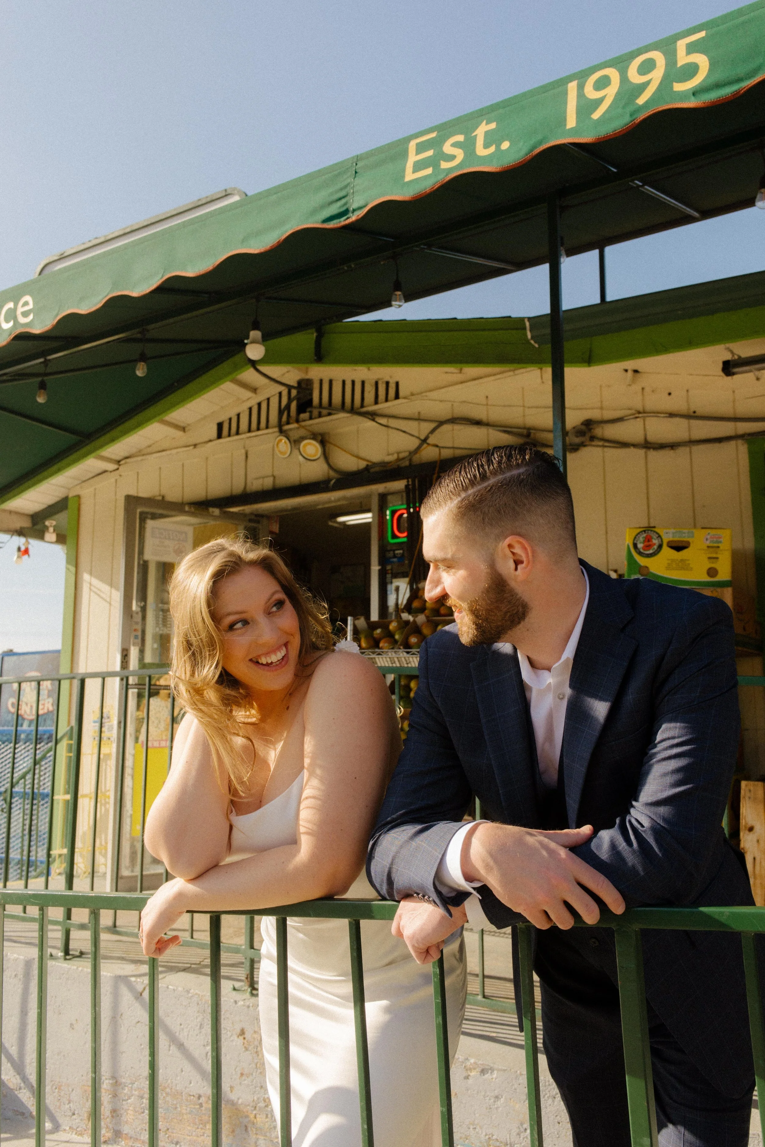 Couple sharing a smile and leaning on a green railing under sunny skies — relaxed and real, just like their San Diego love story.