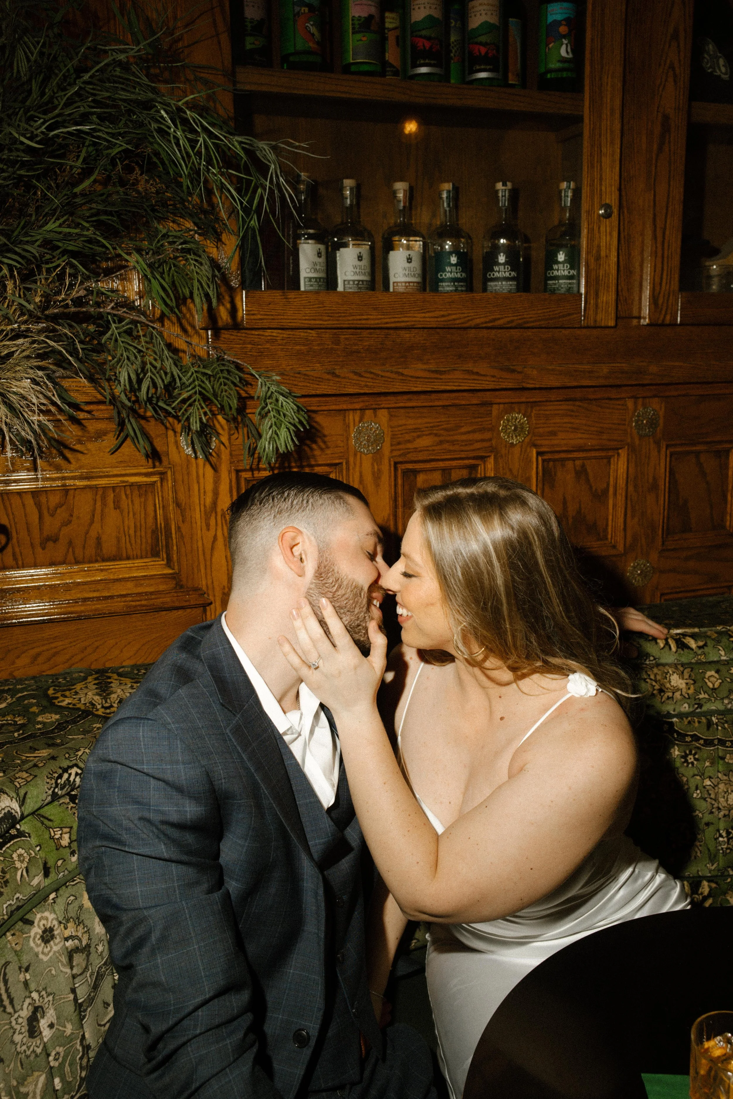 In a moody vintage bar, she cups his face and leans in — a romantic and cozy San Diego engagement photo moment.
