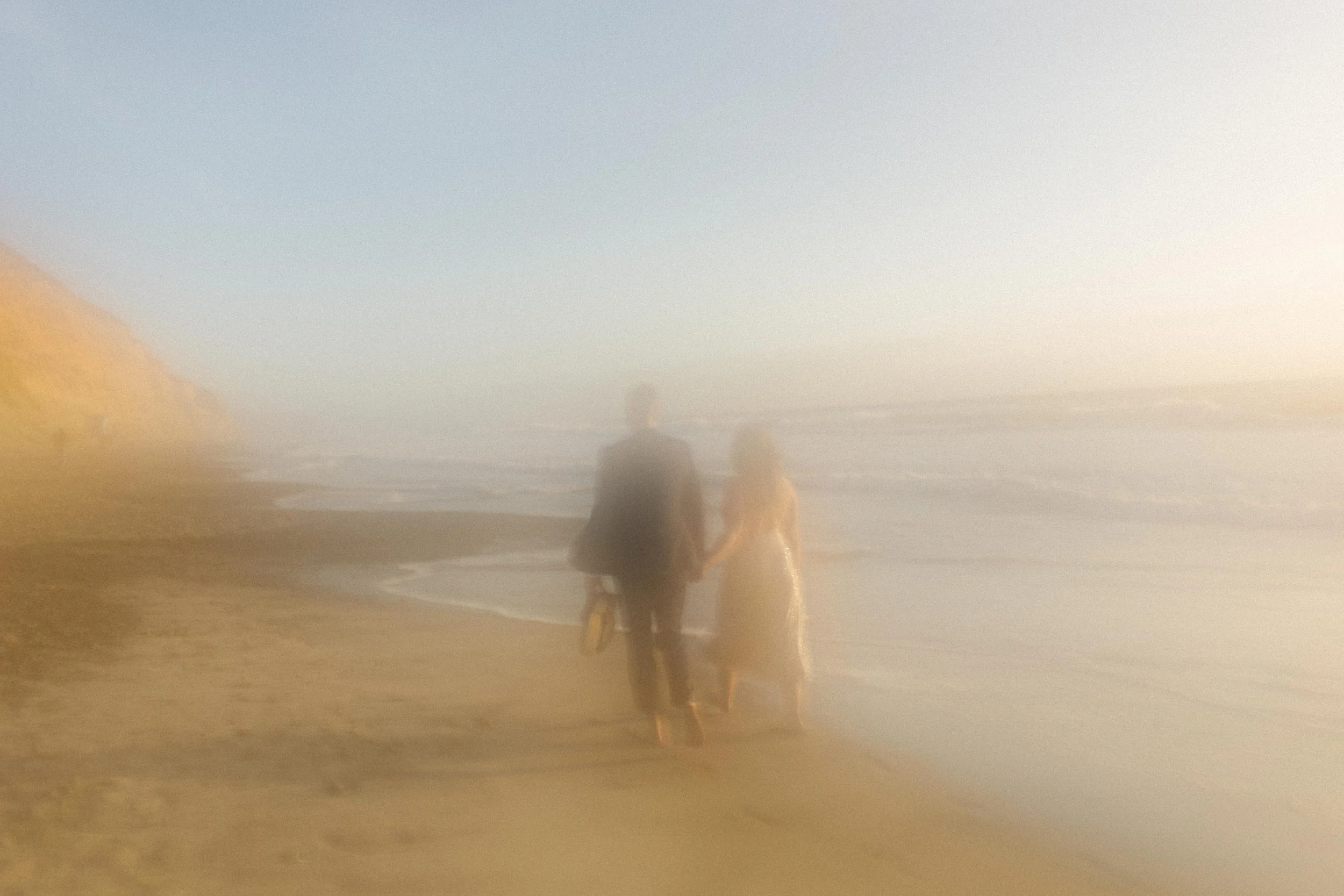 Dreamy and blurred, the couple walks hand-in-hand along the shoreline, a cinematic moment from their San Diego engagement photos.