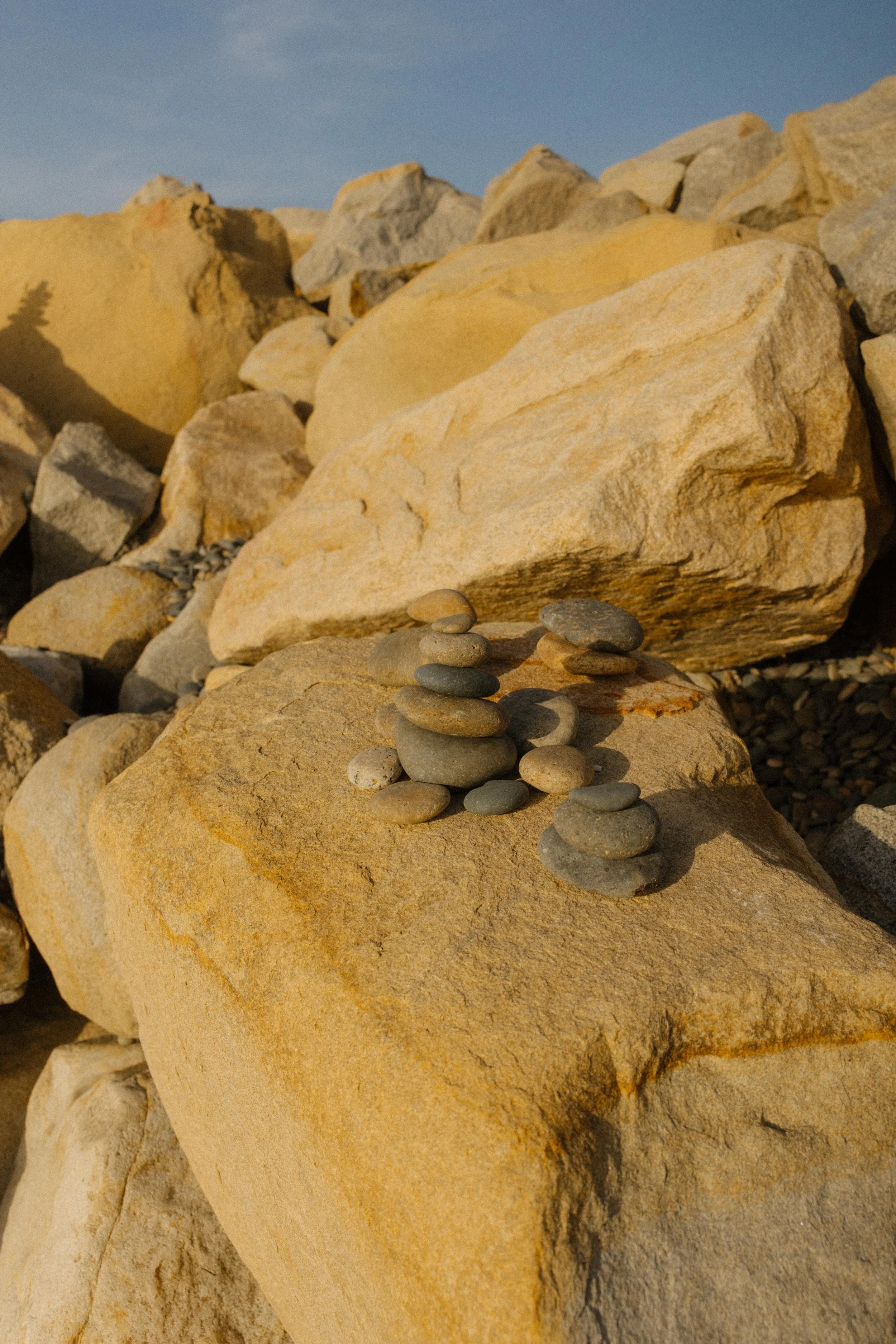 A peaceful little cairn rests on a sun-drenched boulder, grounding the chaos of the coast with a whisper of stillness.