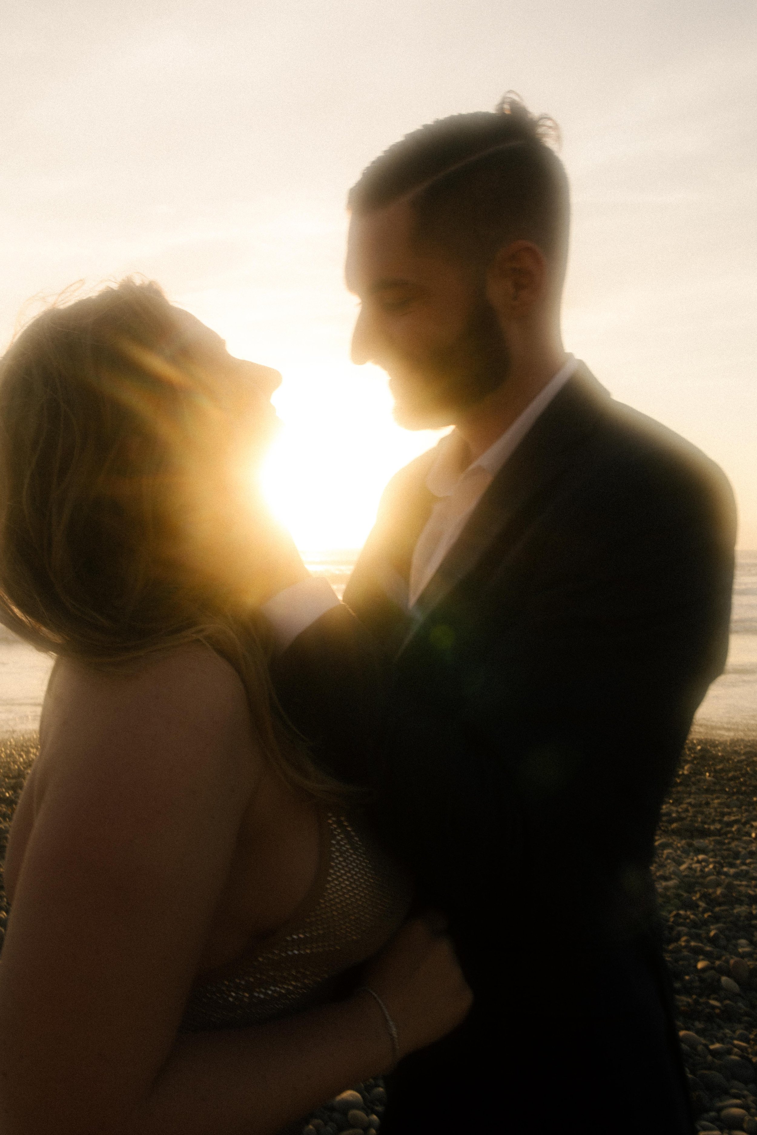 The sun flares between them as they lean in close, her laughter glowing — a cinematic, intimate San Diego engagement photo.