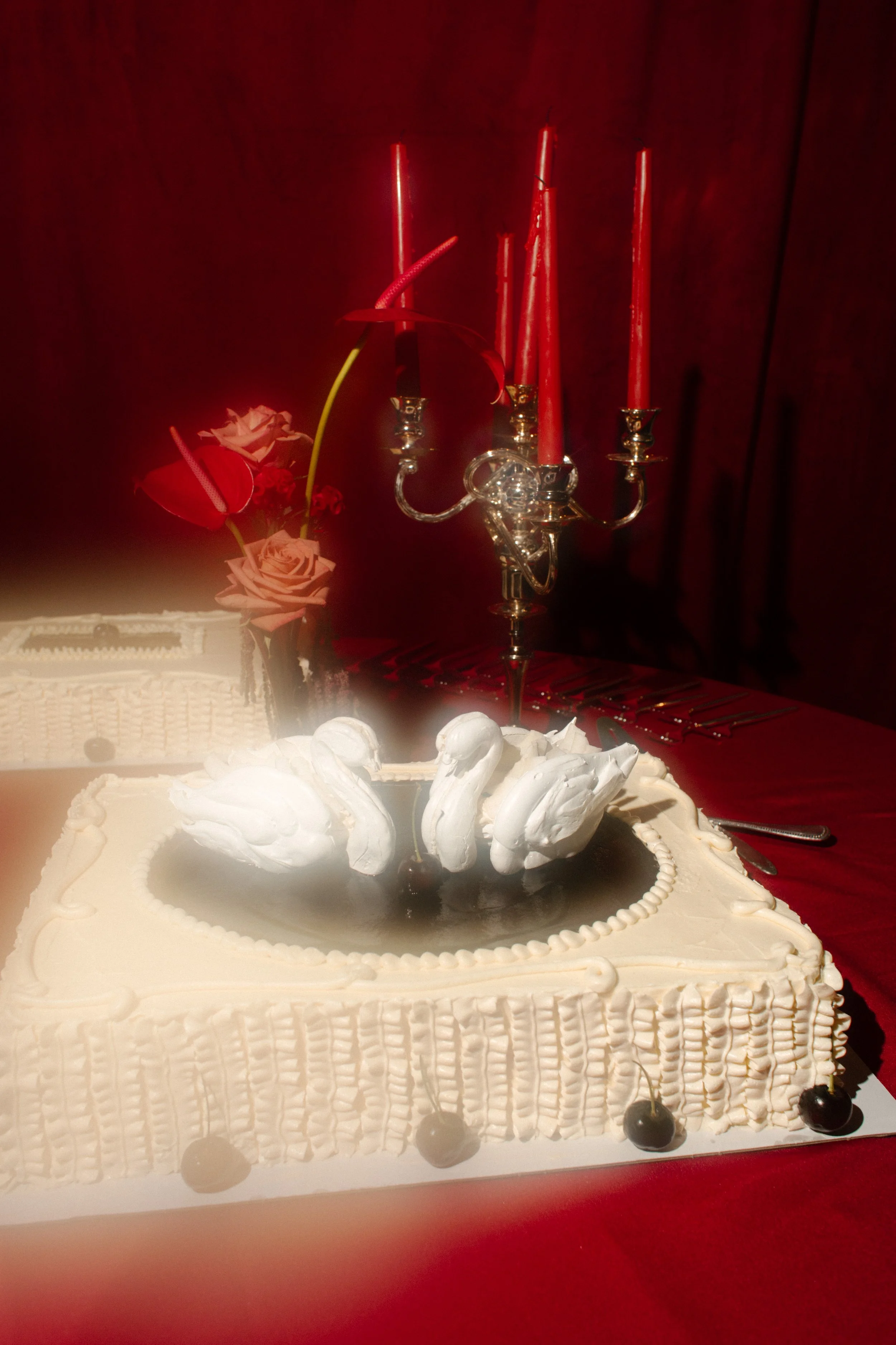 Close-up of a unique swan-topped wedding cake with red candlelight in the background