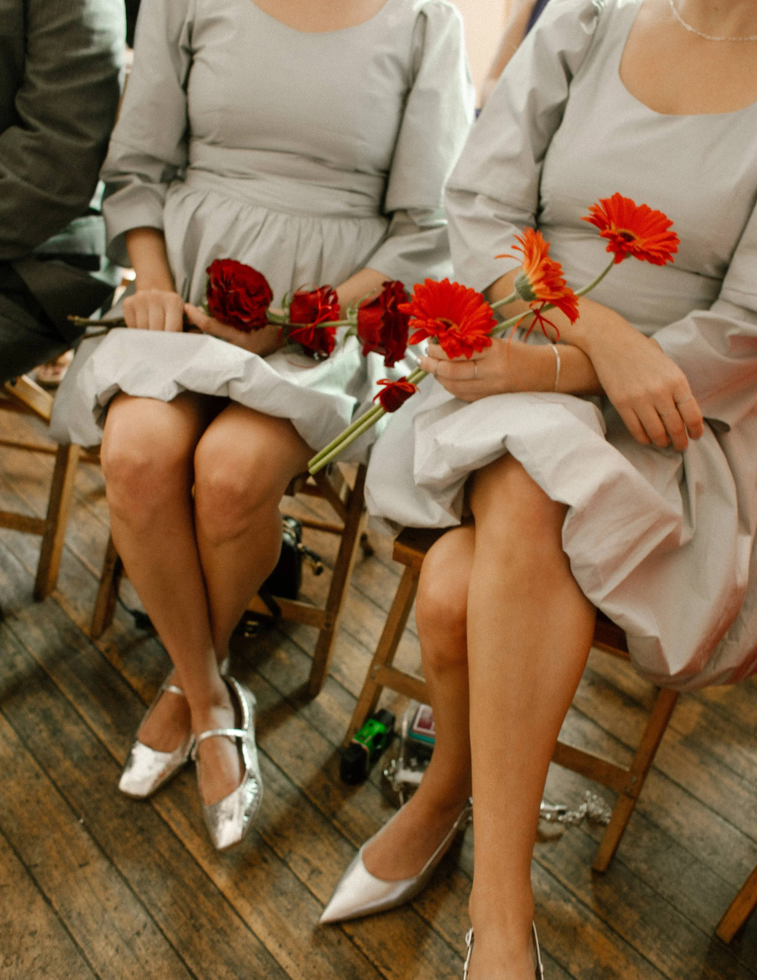 Bridesmaids in silver dresses holding bold red flowers while seated during the ceremony