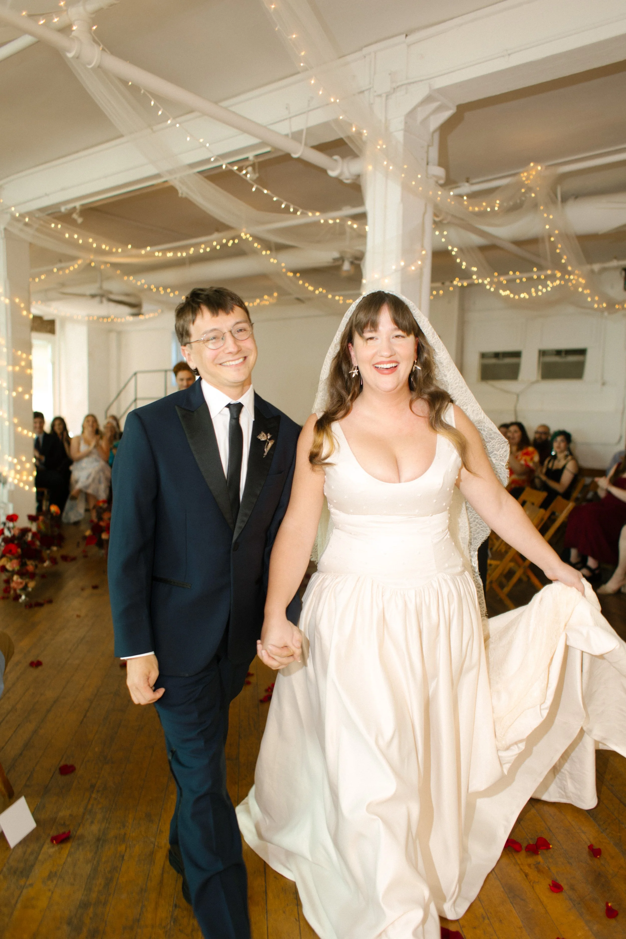 The newlyweds walk back down the aisle beaming, surrounded by cheers and petals