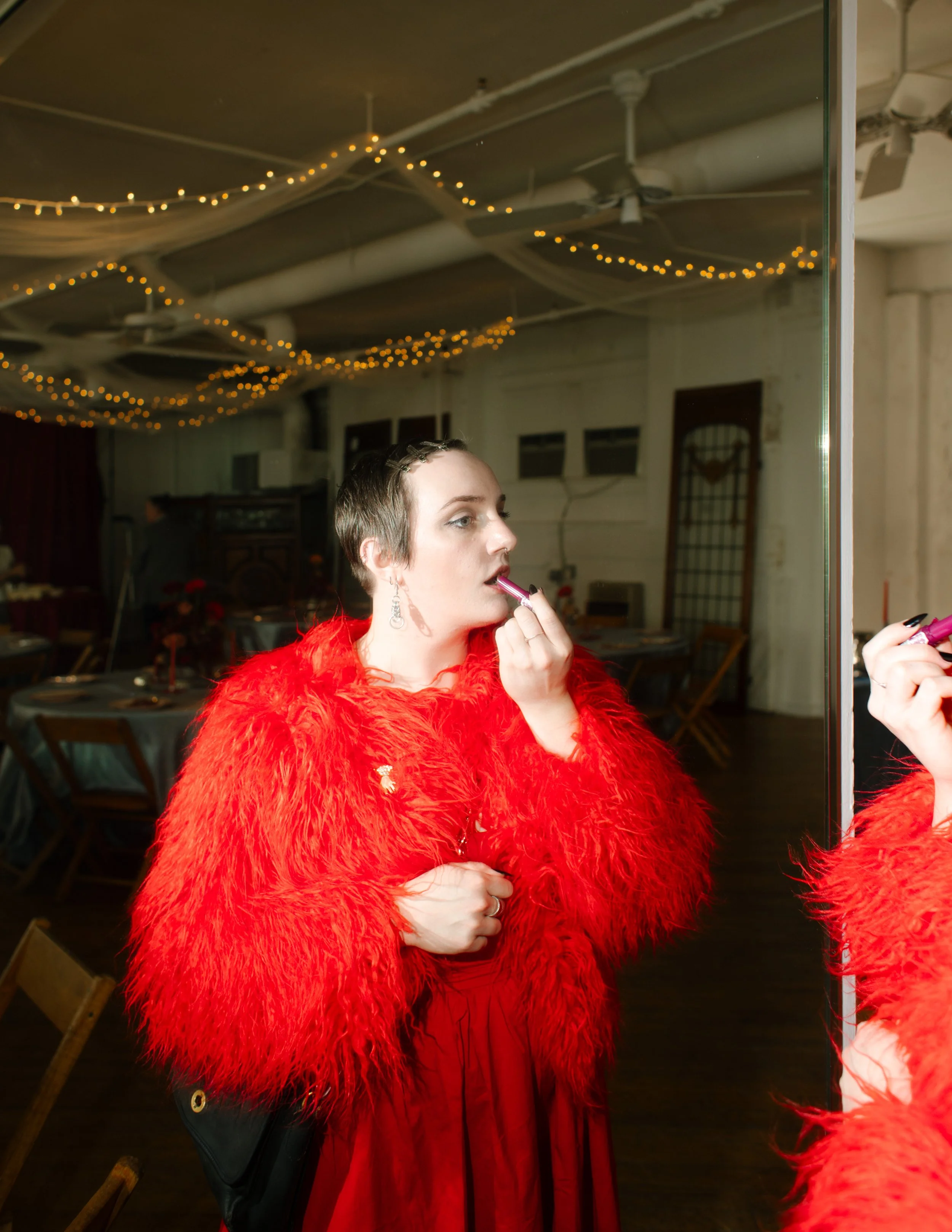 Tennessee wedding guest touches up lipstick in mirror while wearing bright red fluffy jacket