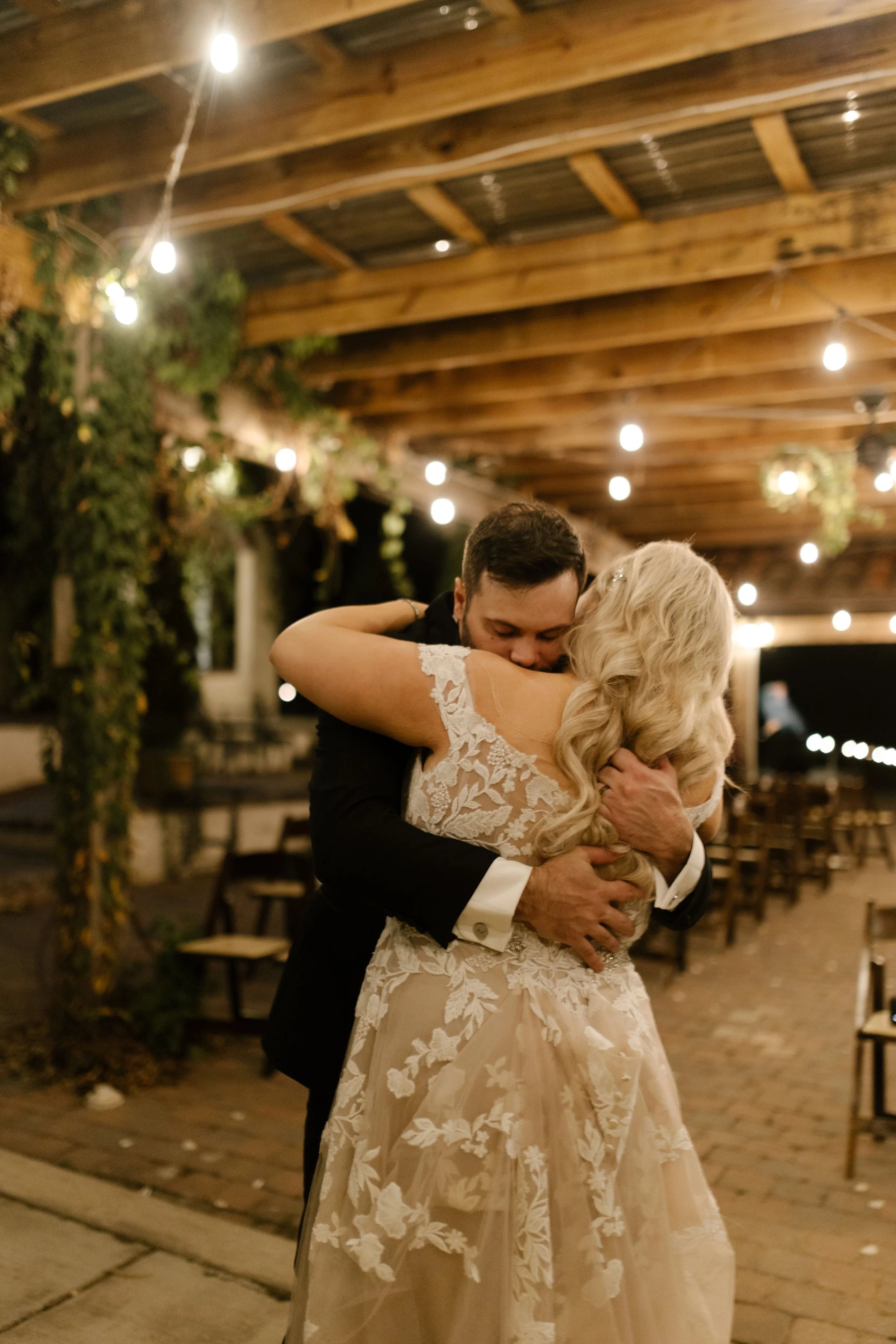 Bride and groom embracing under string lights during their italy inspired wedding reception with warm, romantic evening ambiance.