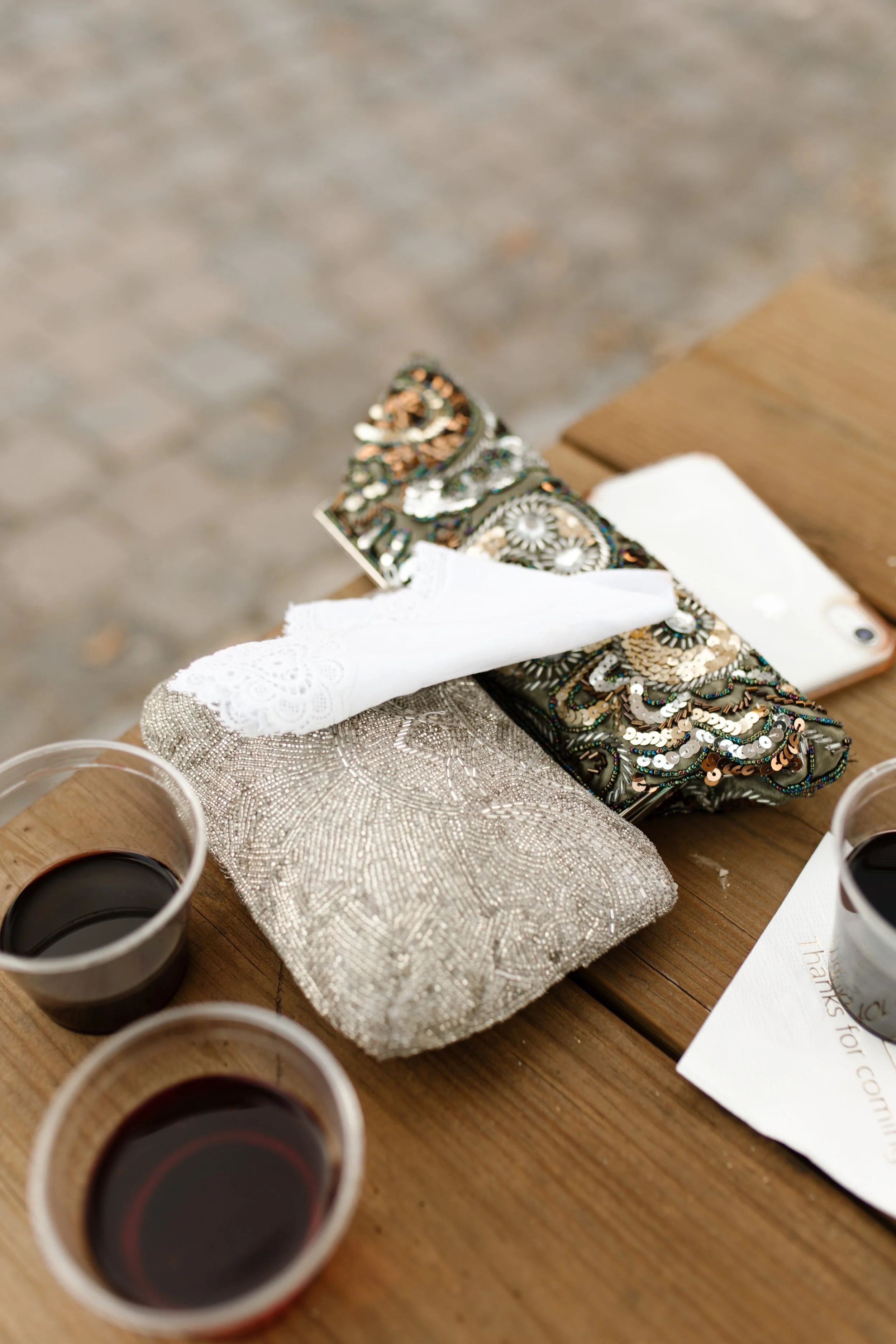Beaded bridal clutch and glasses of red wine resting on a wooden table at an italy inspired wedding reception with warm, rustic details.