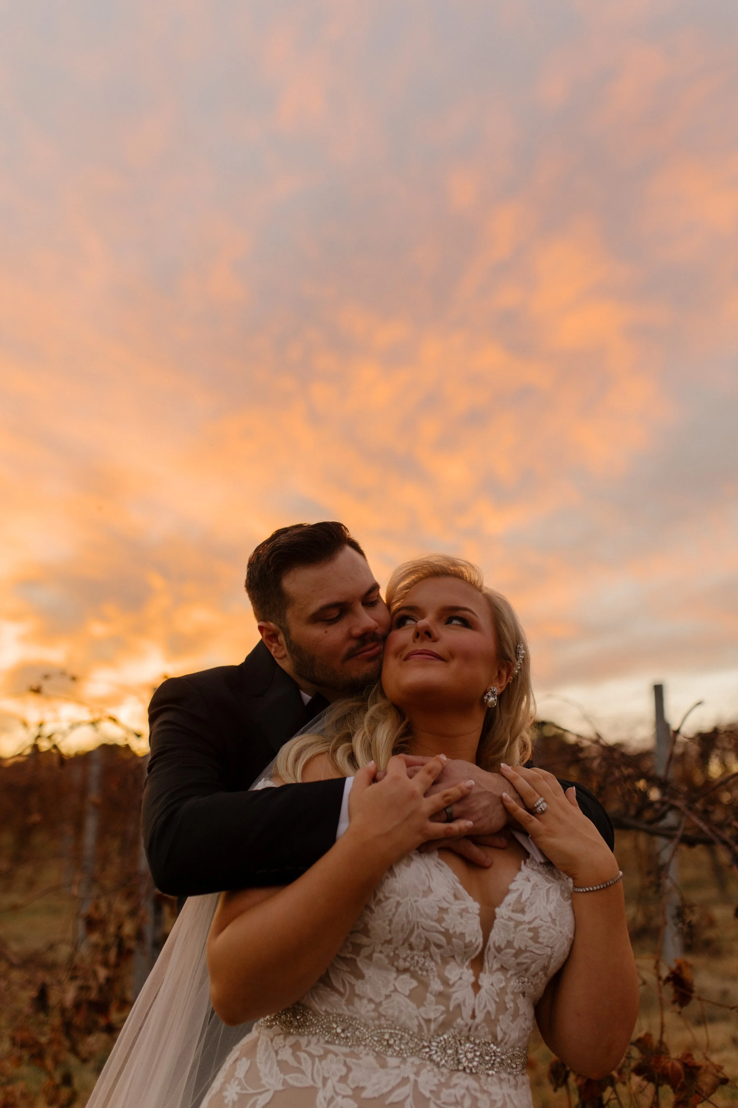 Bride and groom embracing in a vineyard at sunset during their italy inspired wedding, with warm golden skies and rolling vines in the background.