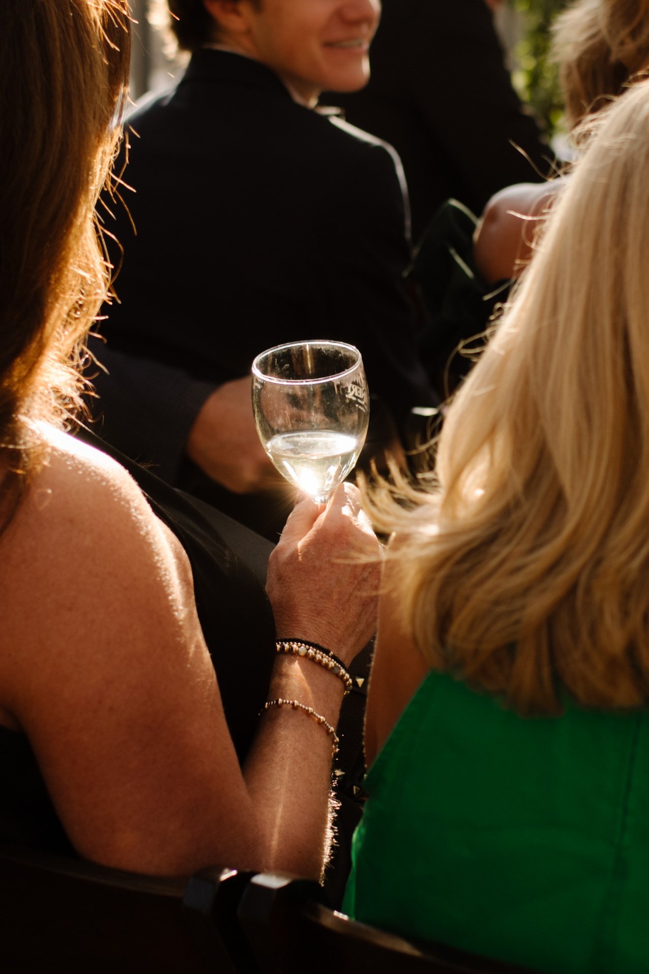 Wedding guest holding a glass of white wine in golden sunset light during an italy inspired wedding celebration with warm, candid atmosphere.