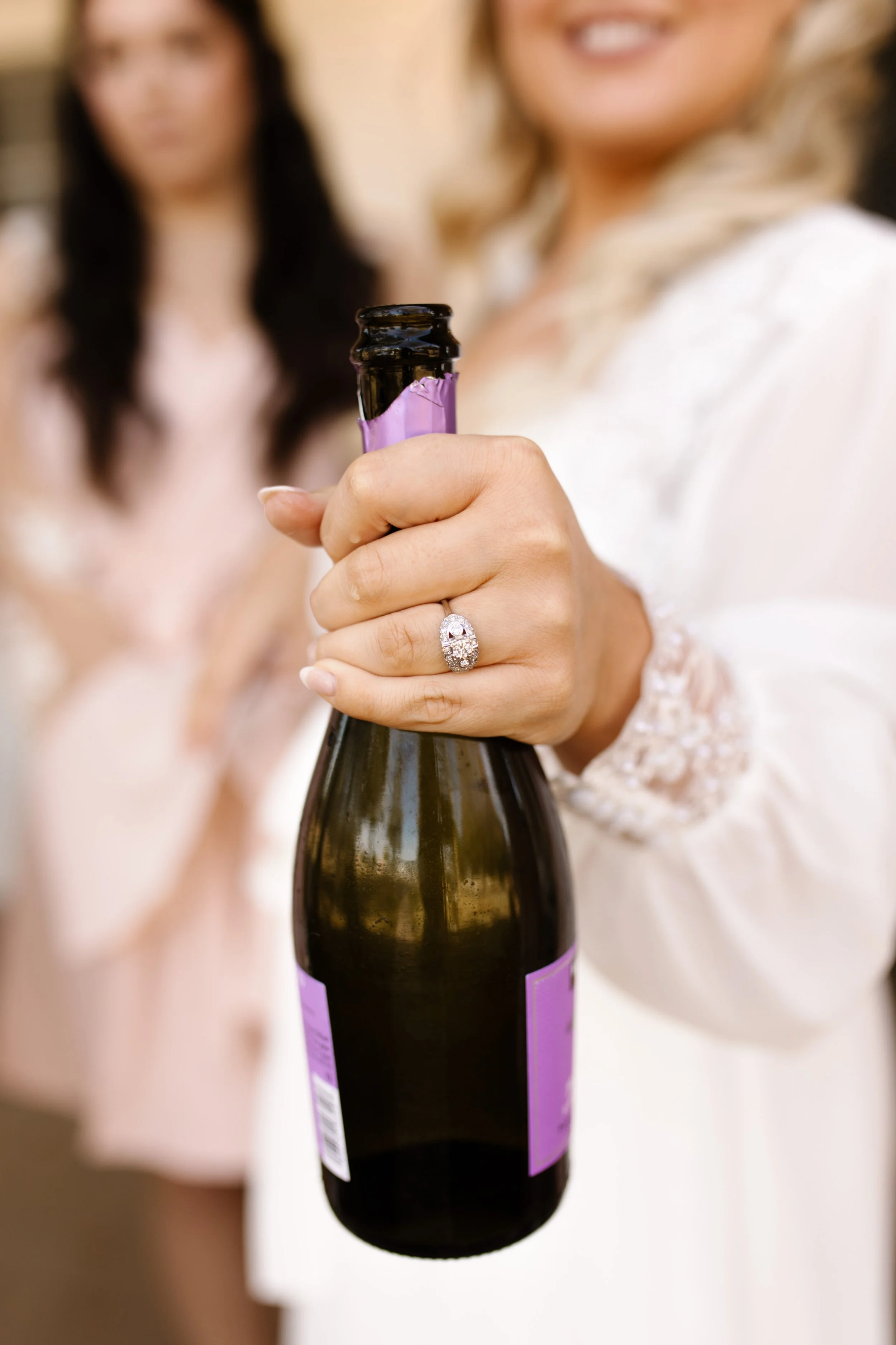 Bride popping a champagne bottle, engagement ring sparkling, during a joyful italy inspired wedding getting-ready celebration.