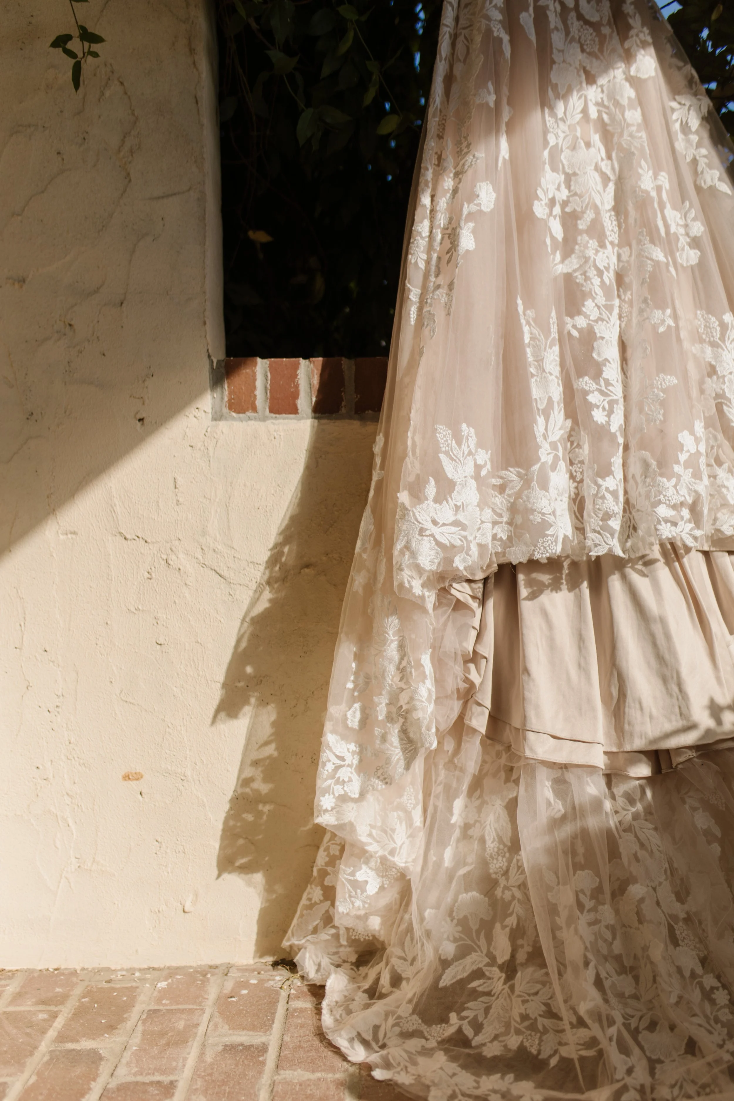Lace wedding gown cascading against a stucco wall with brick accents at an italy inspired wedding venue.
