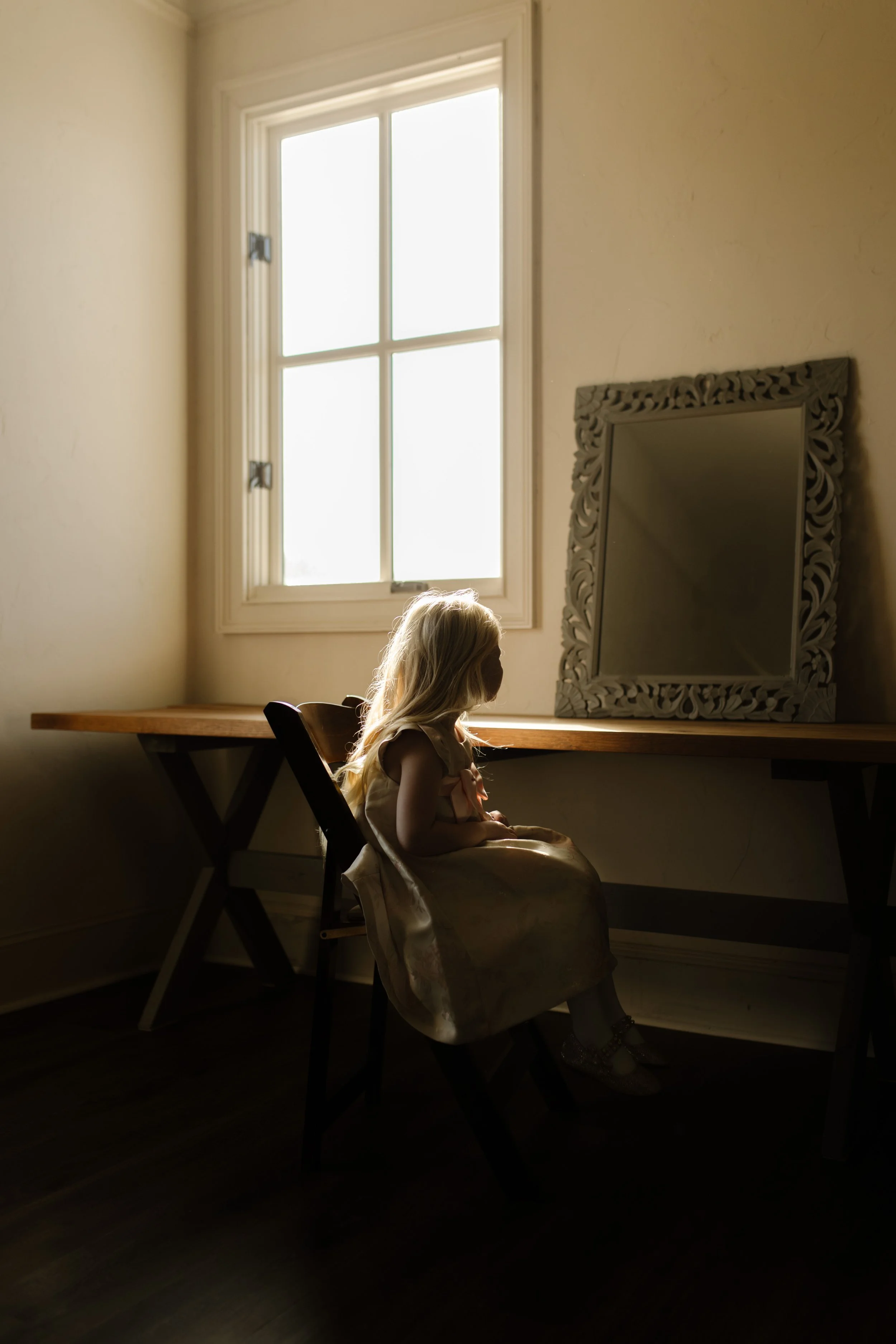 Flower girl sitting by a sunlit window in soft golden light during a quiet moment at an italy inspired wedding morning.