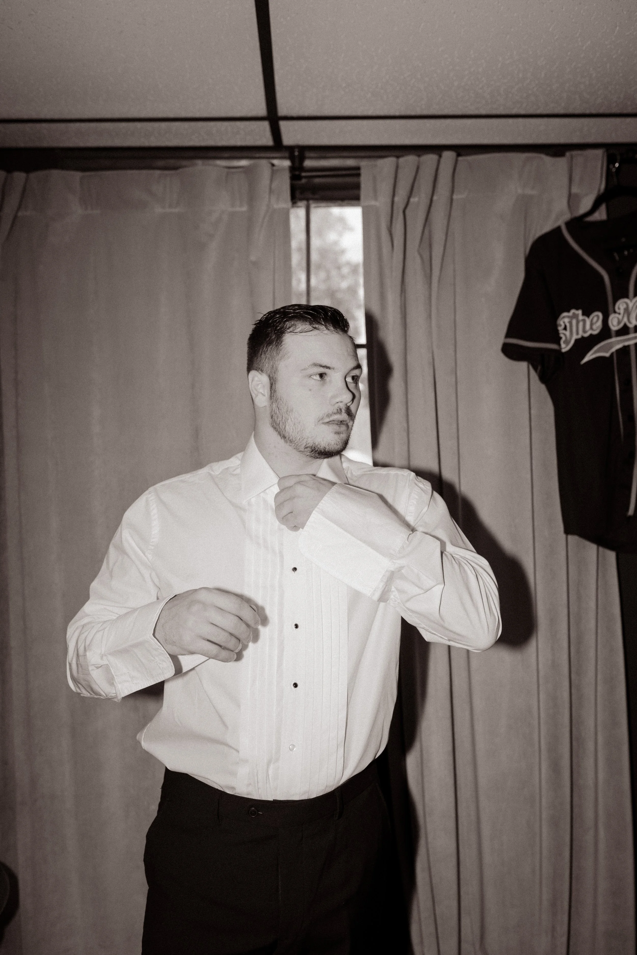 Black and white portrait of the groom adjusting his shirt cuffs while preparing for his wedding day