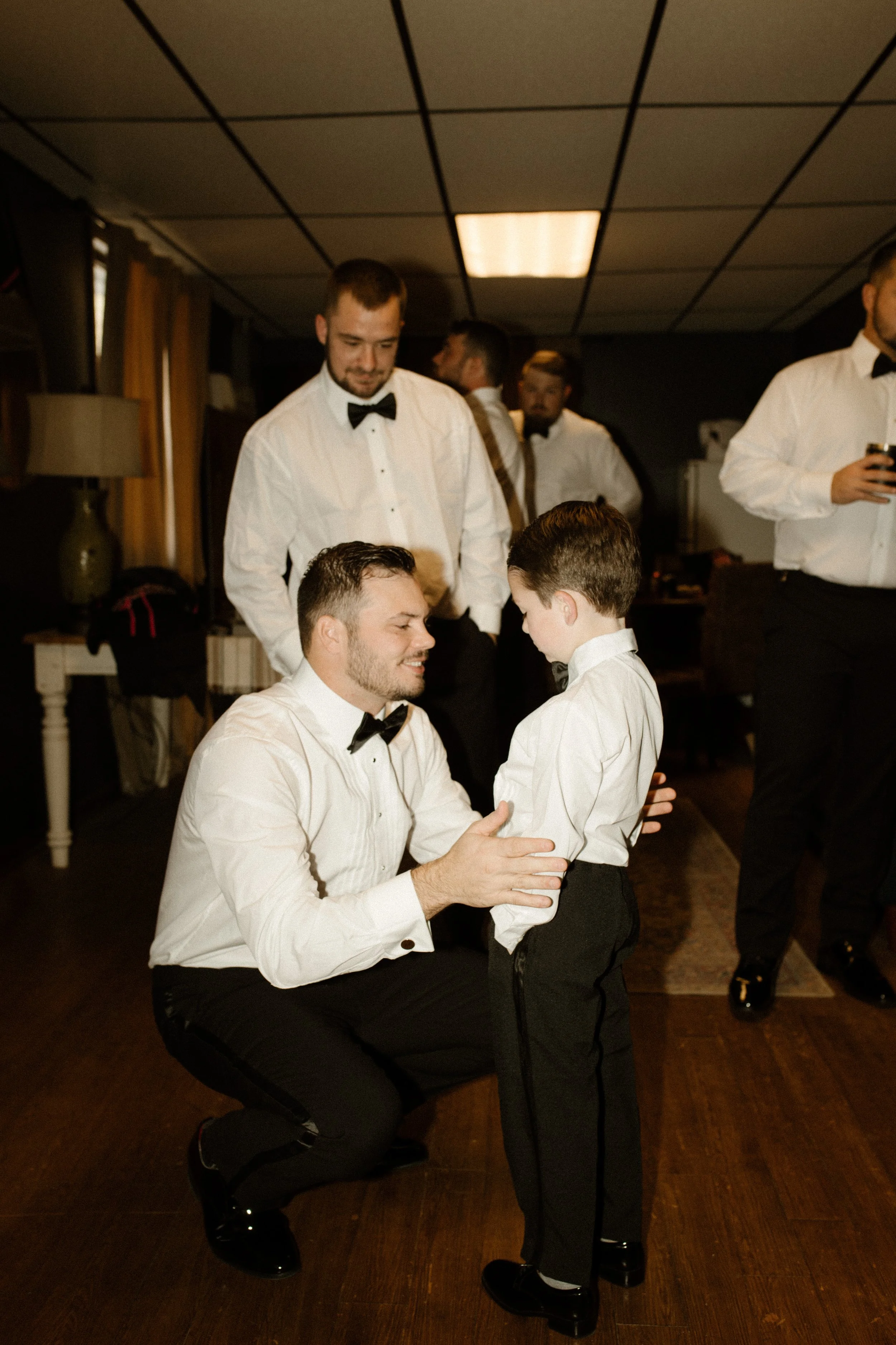 Groom kneeling to talk with the young ring bearer while getting ready for an italy inspired wedding in a warm, candid behind-the-scenes moment.