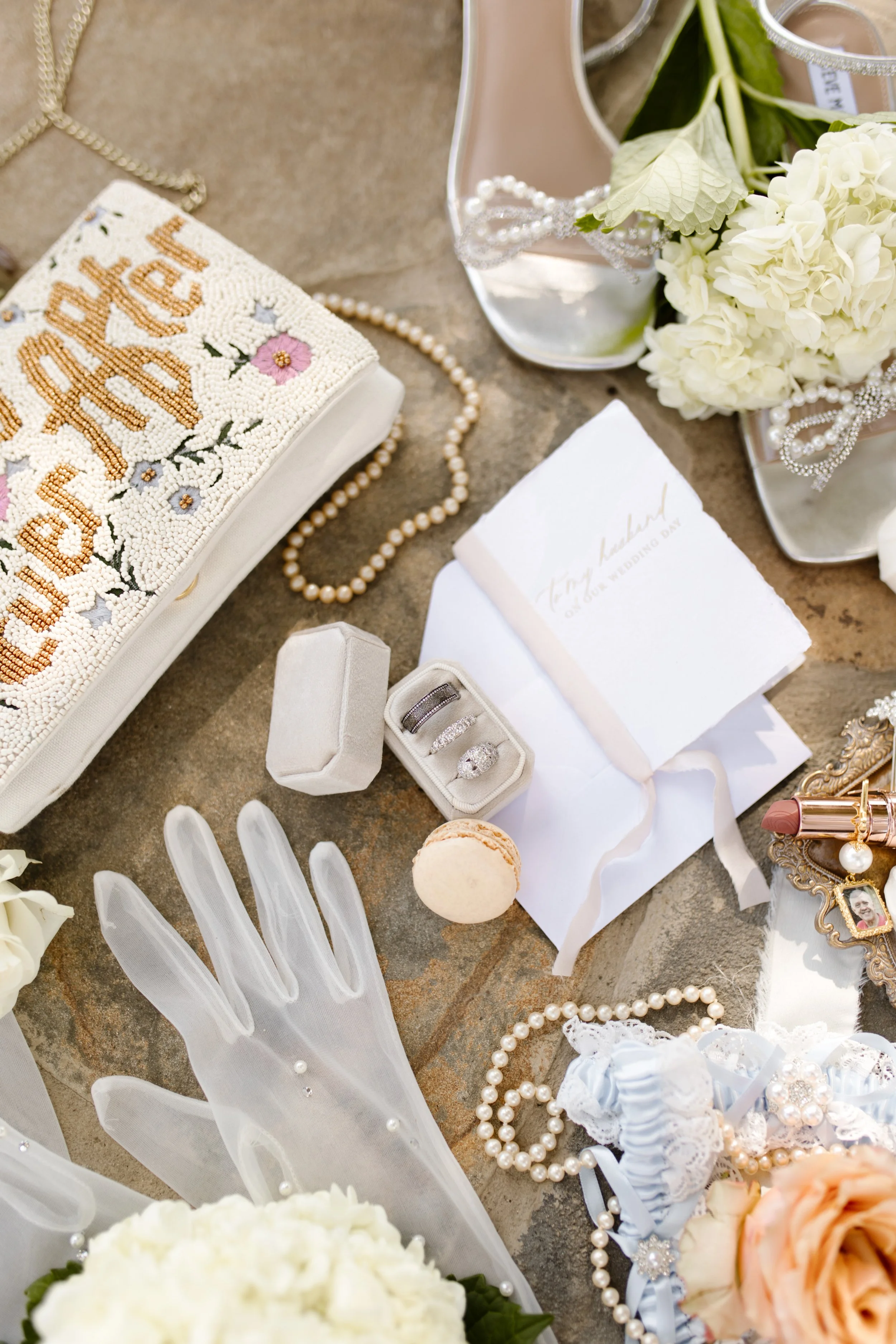 Bridal detail flat lay featuring pearl heels, heirloom jewelry, wedding rings, embroidered clutch, and soft florals at an italy inspired wedding.