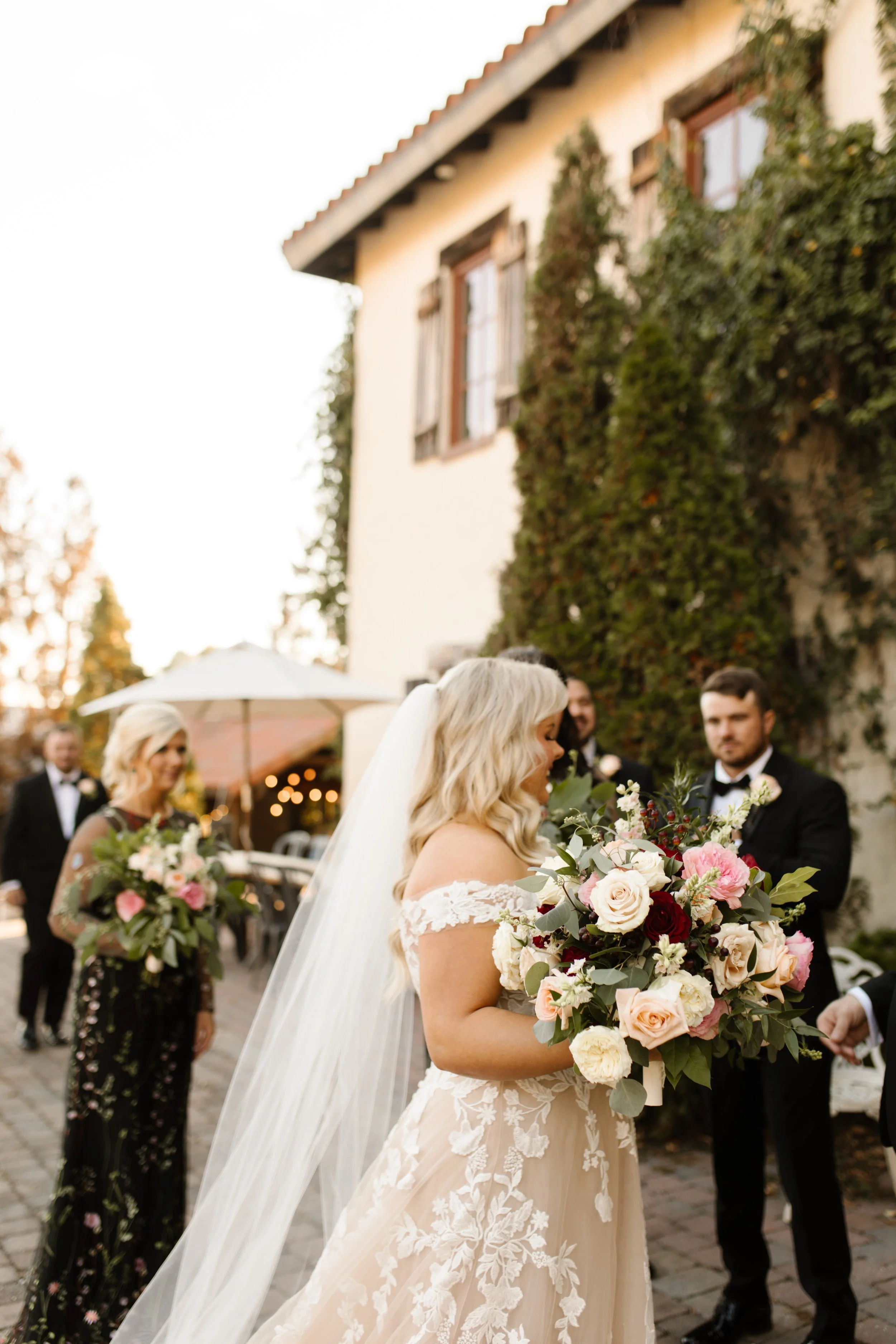 Bride holding a lush bouquet while bridesmaids and groomsmen gather behind her outside an ivy-covered villa during an italy inspired wedding.