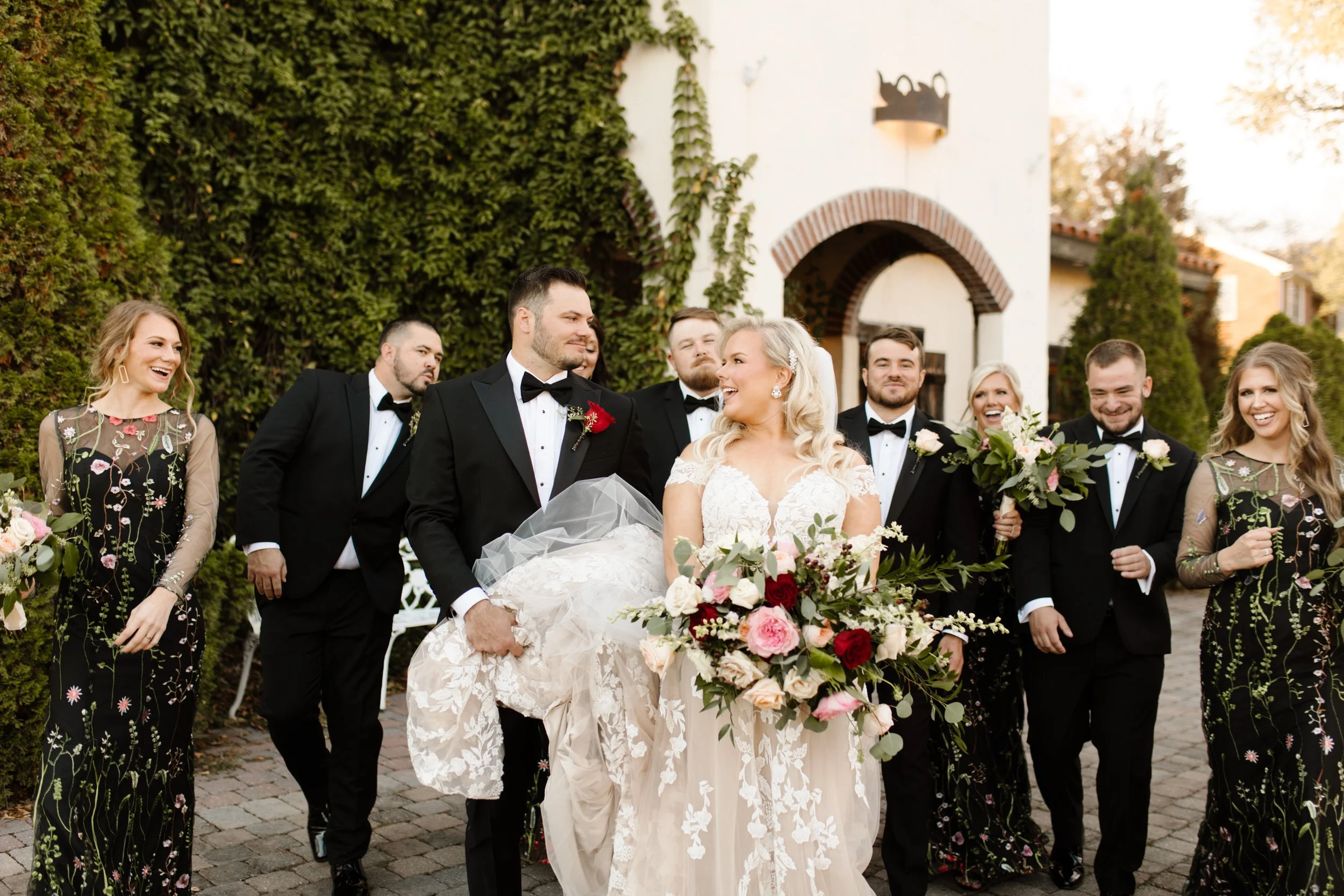 Bride and groom walking with their full wedding party in front of an ivy-covered Mediterranean-style venue during an italy inspired wedding.