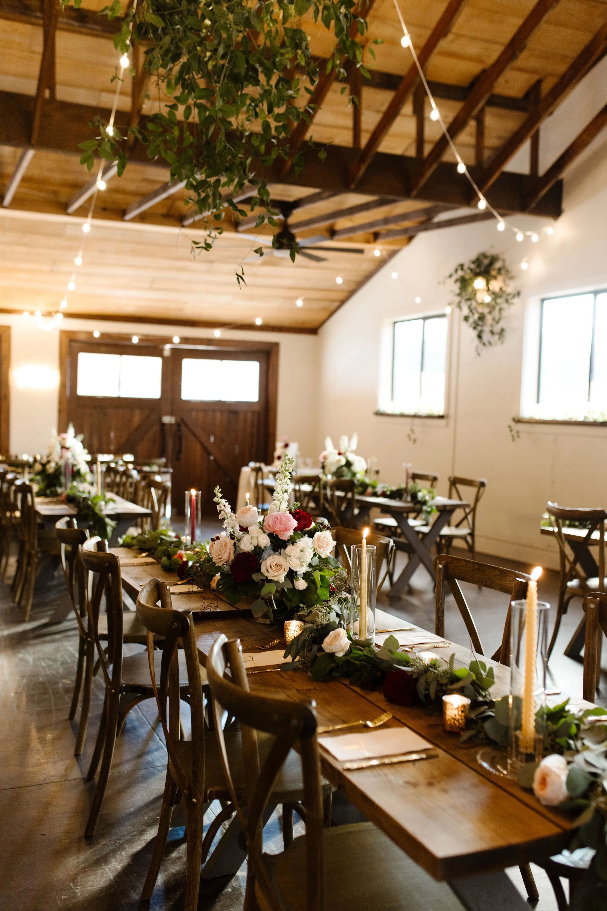 Long wooden reception tables beneath hanging greenery and string lights at a warm, candlelit italy inspired wedding venue.