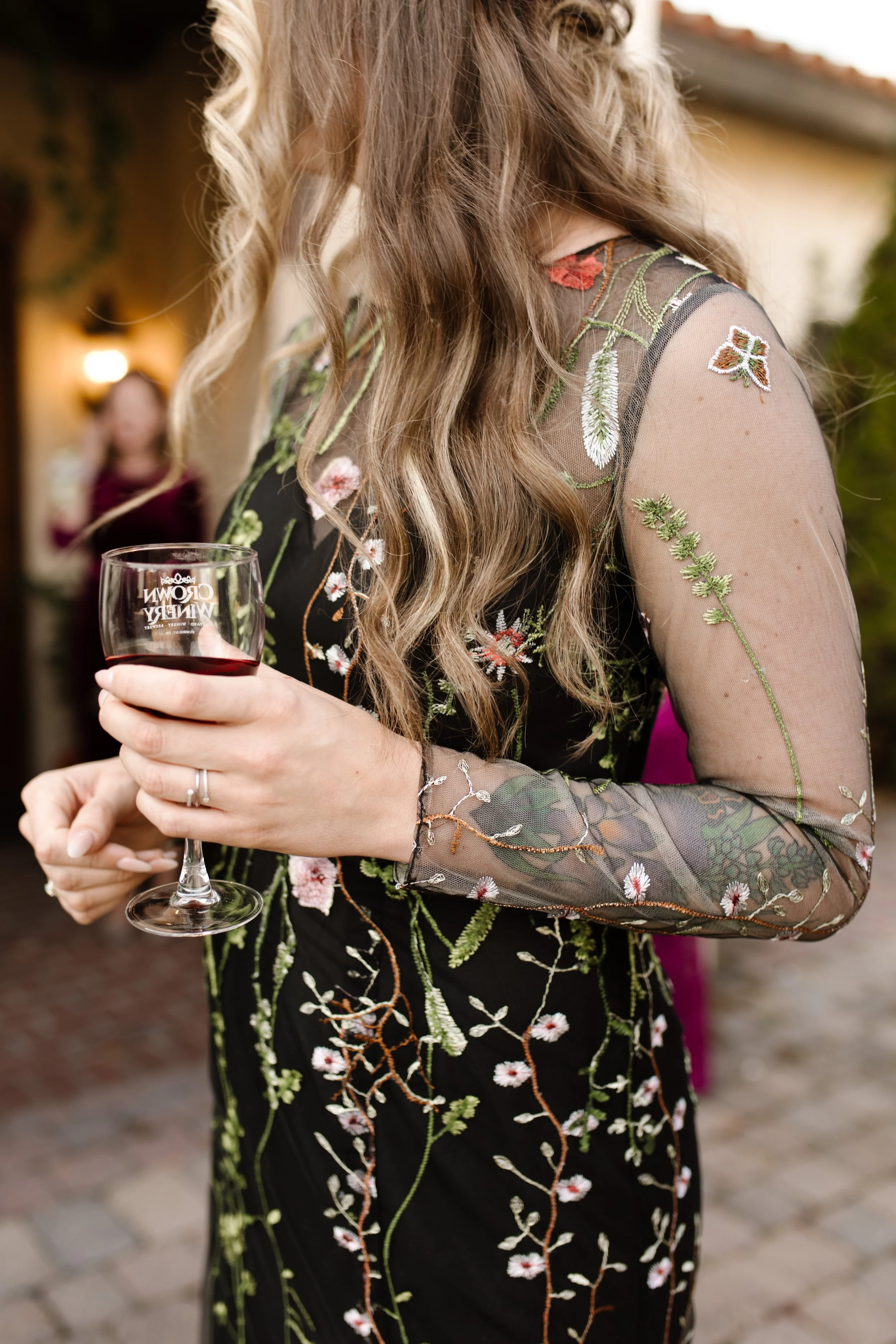 Wedding guest in a black embroidered dress holding a glass of red wine during an italy inspired wedding celebration.