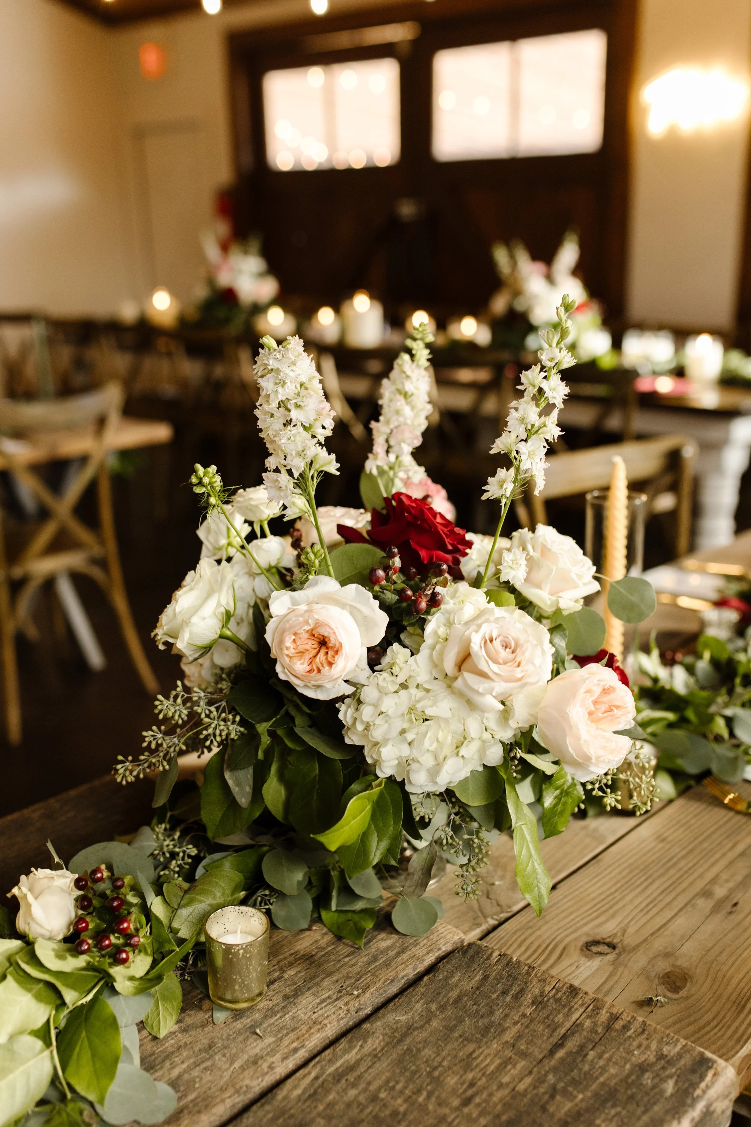 Romantic floral centerpiece with blush roses, white blooms, greenery, and candlelight on a wooden table at an italy inspired wedding reception.