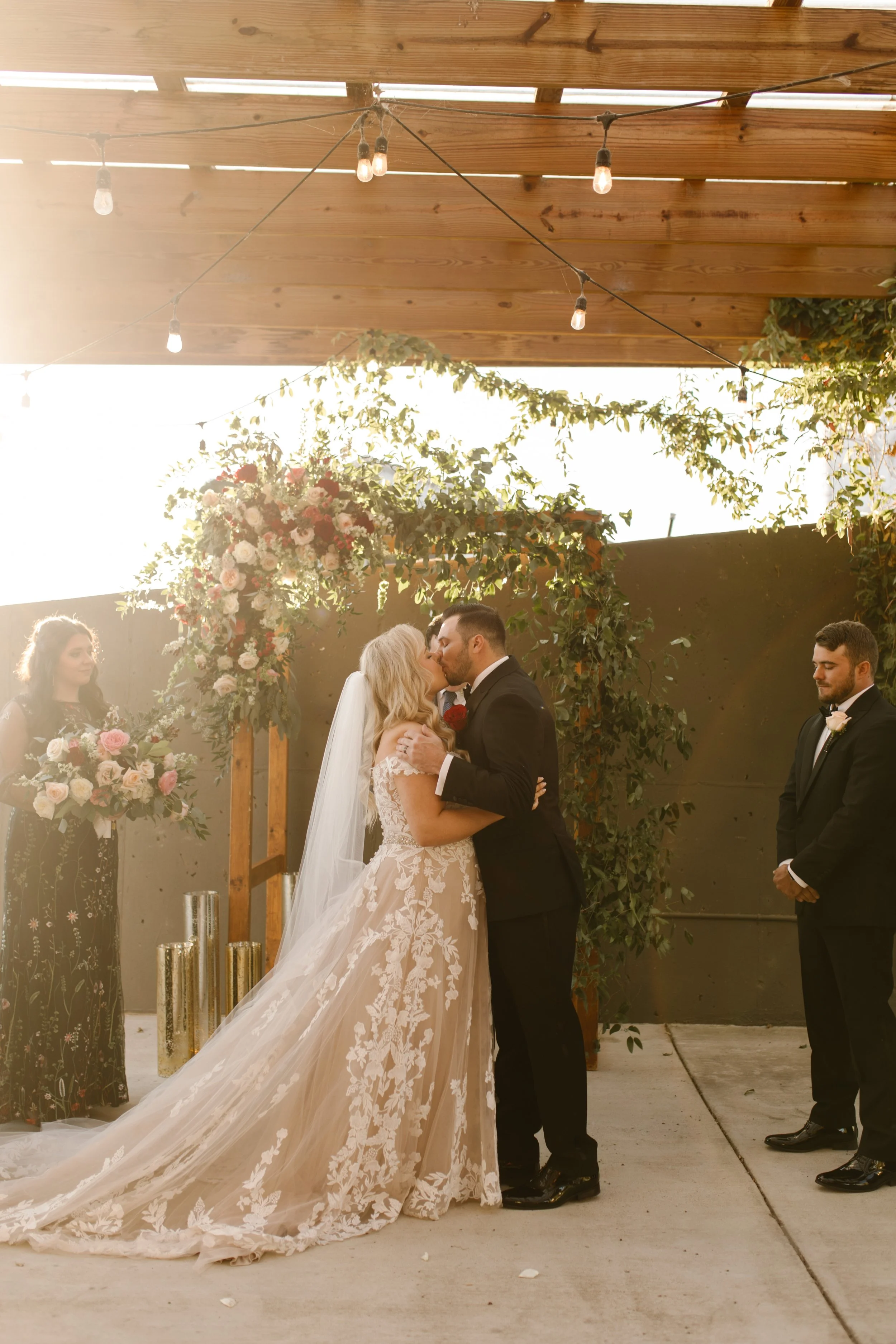 Bride and groom kissing beneath a floral arch in warm golden light at their italy inspired wedding ceremony.