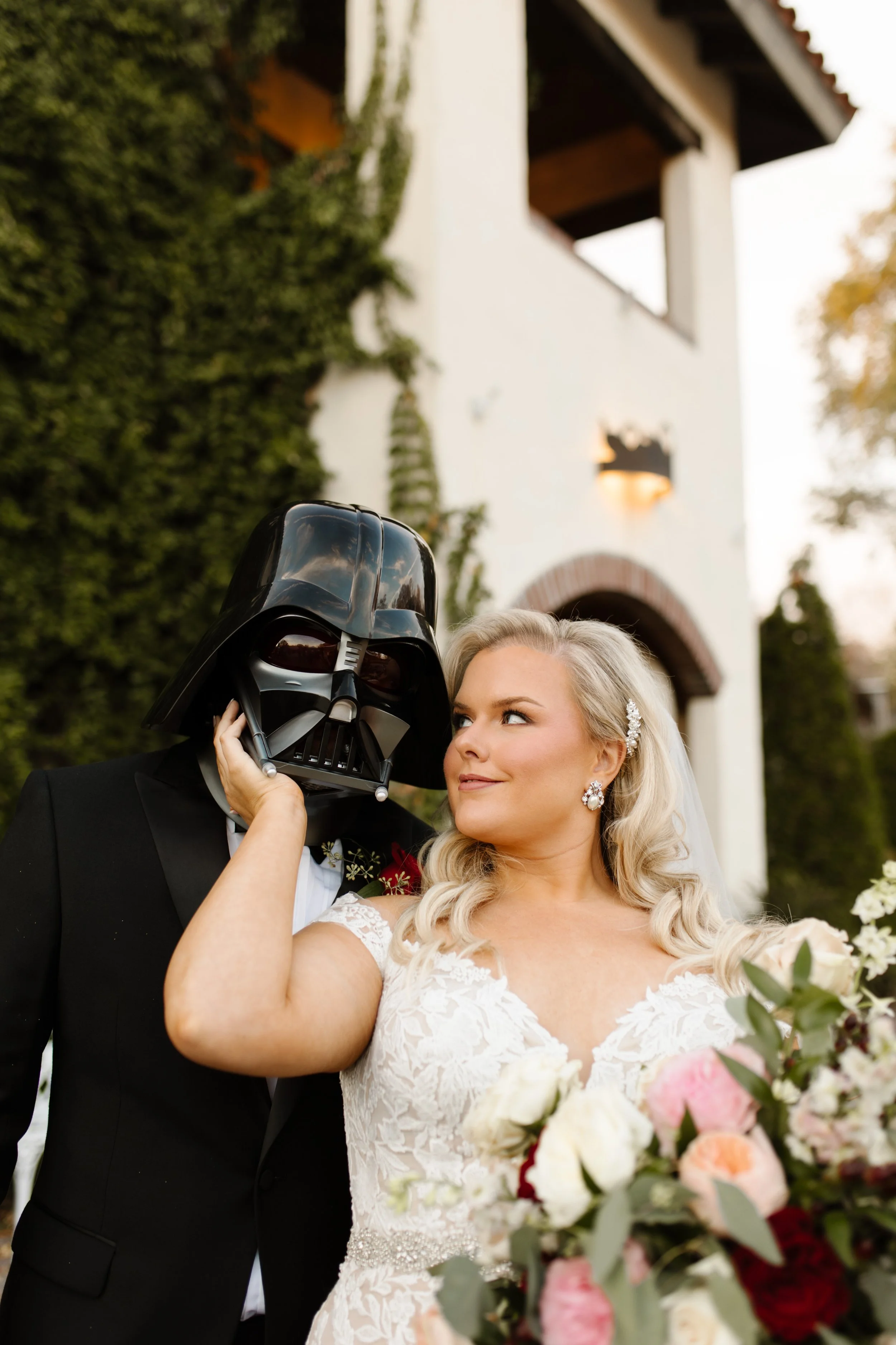 Bride holding the groom’s Darth Vader helmet while posing in front of an ivy-covered villa during a playful italy inspired wedding portrait.