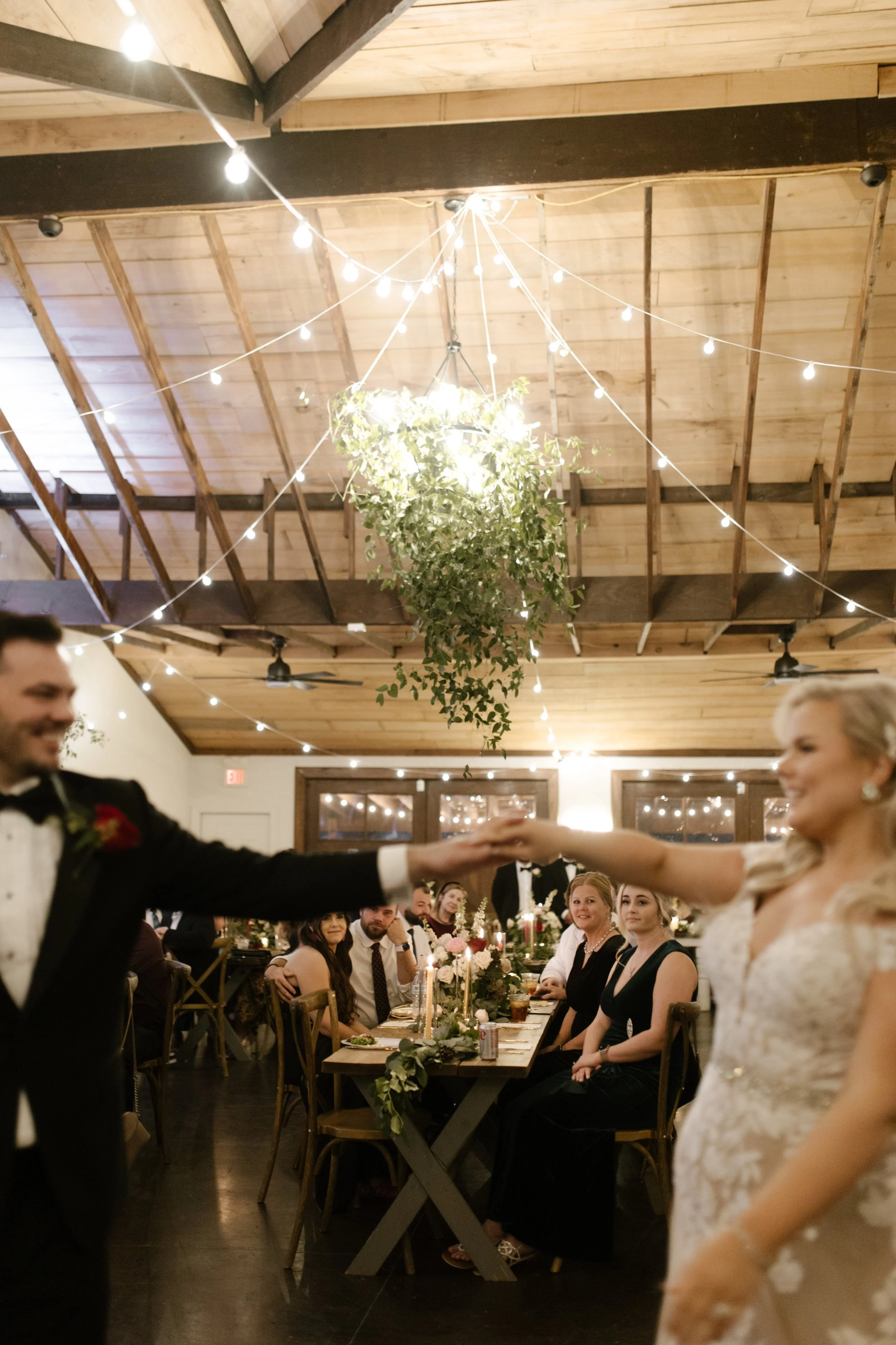 Bride and groom spinning together under string lights during their italy inspired wedding reception in a warm, wood-beamed venue.