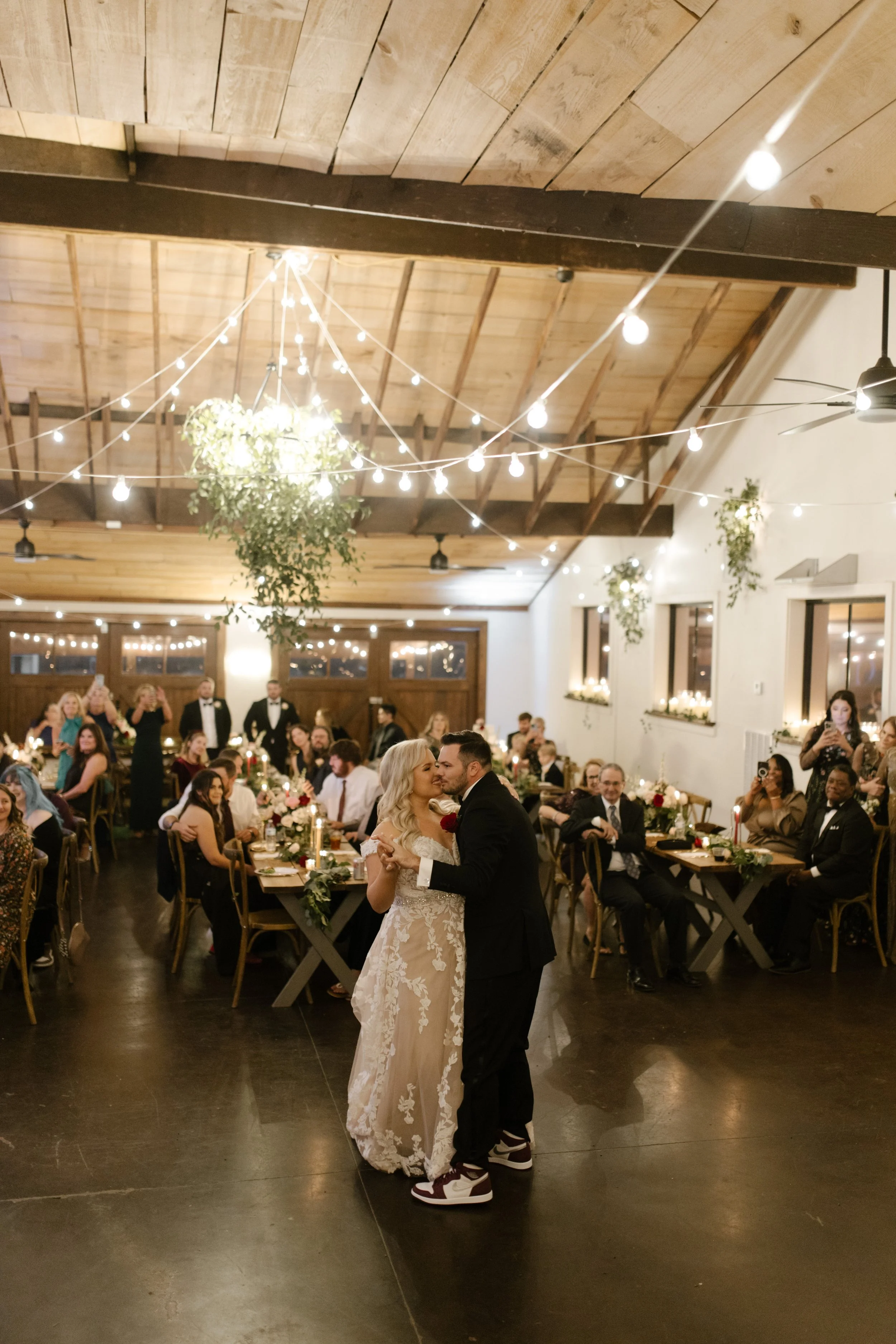 Bride and groom sharing an intimate first dance surrounded by guests at an italy inspired wedding reception with greenery and café lights overhead.