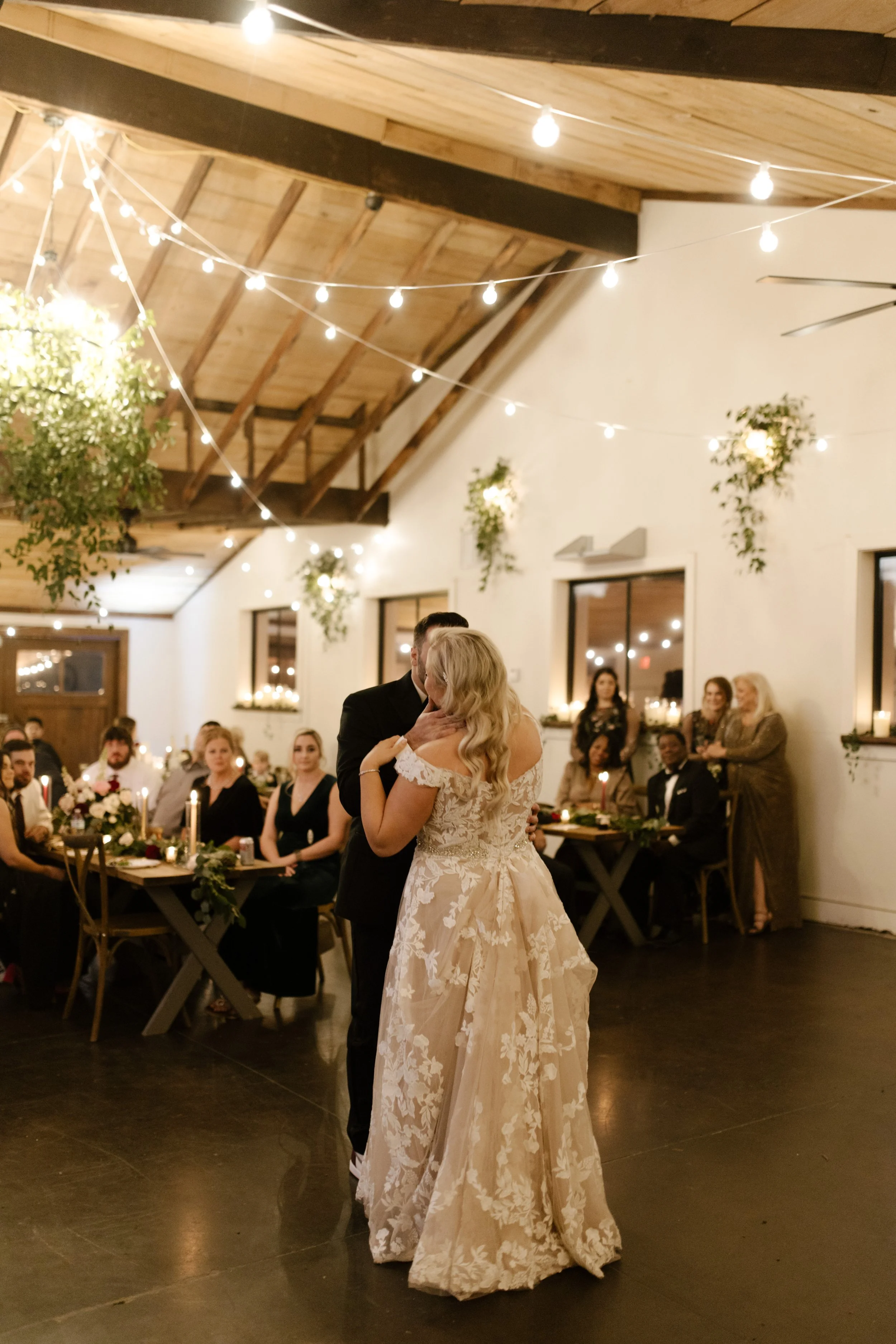 Bride and groom sharing their first dance under string lights in a warm, romantic italy inspired wedding reception space.