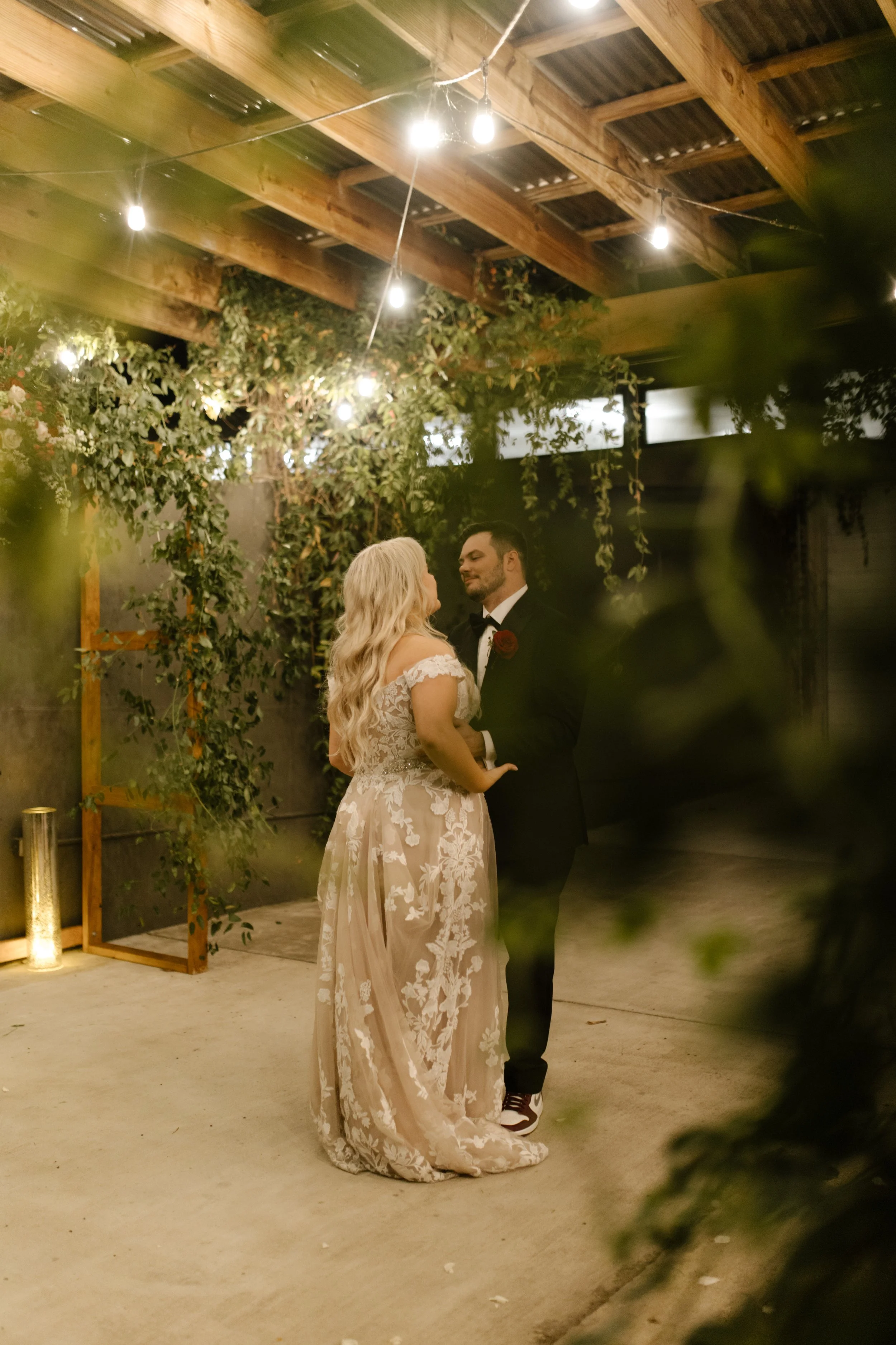Bride and groom standing beneath greenery and string lights during a romantic evening moment at their italy inspired wedding.