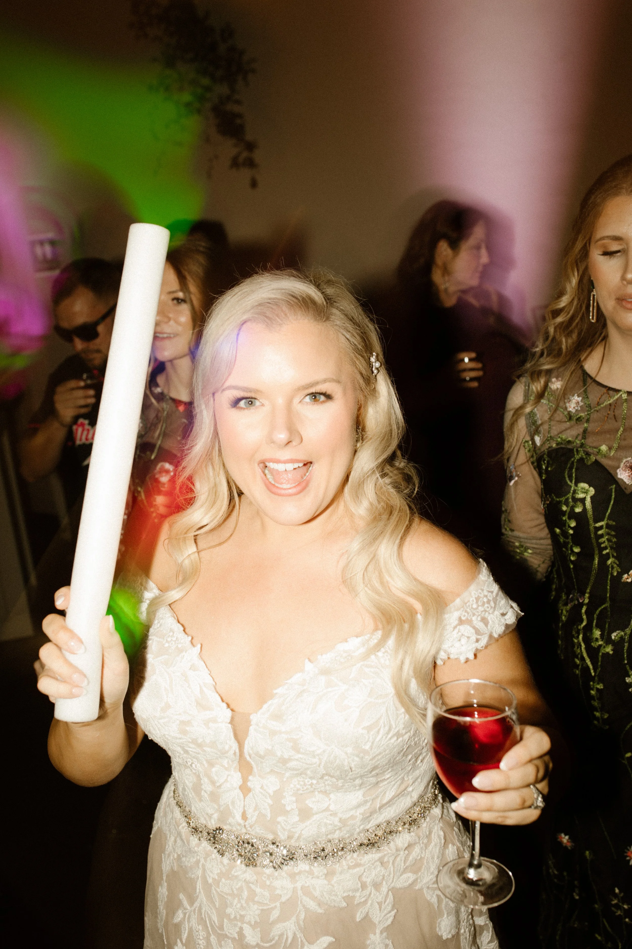 Bride holding a glow stick and glass of red wine while dancing at her italy inspired wedding reception.