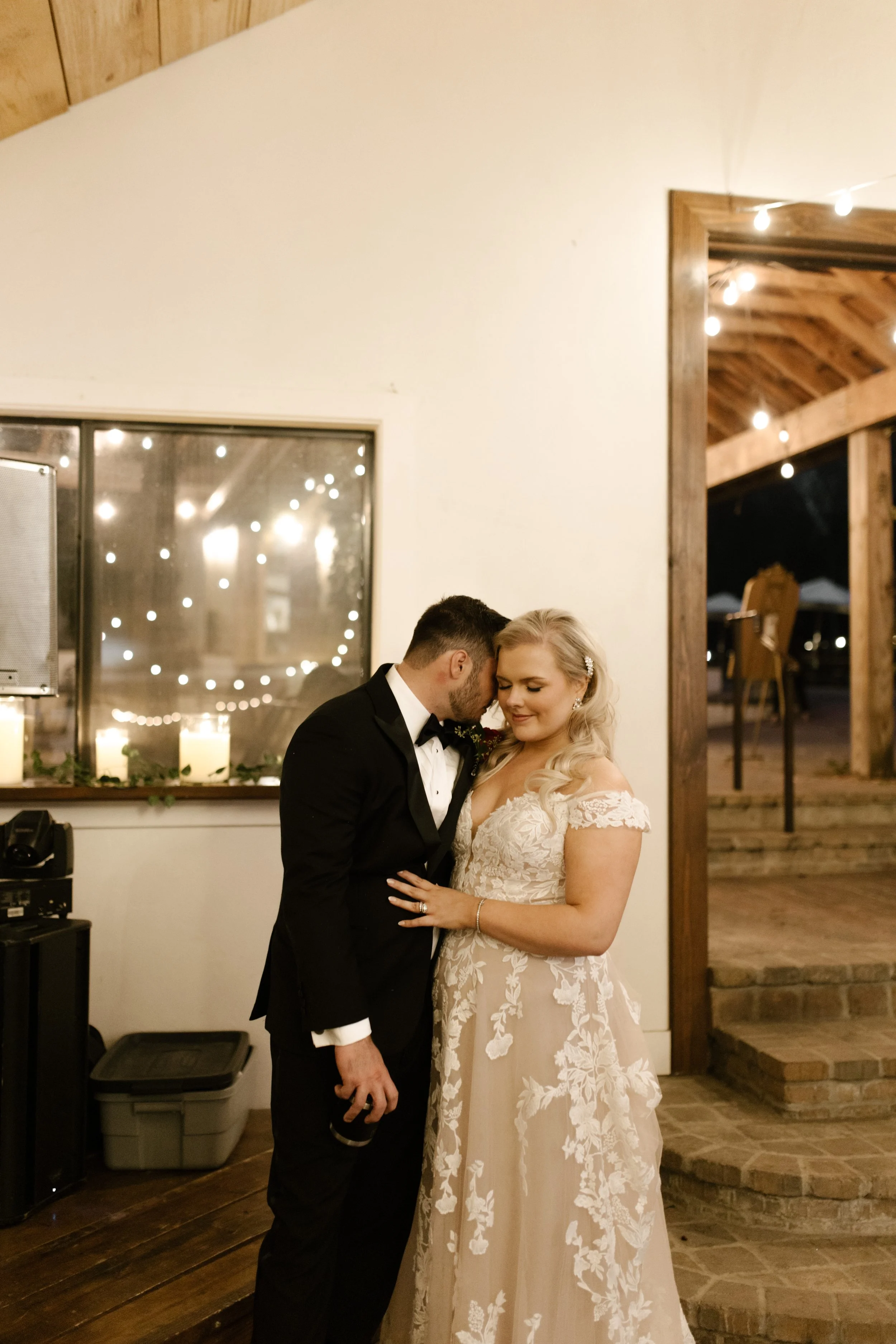 Bride and groom sharing a quiet embrace inside their italy inspired wedding reception space with warm candlelight and wooden beams.