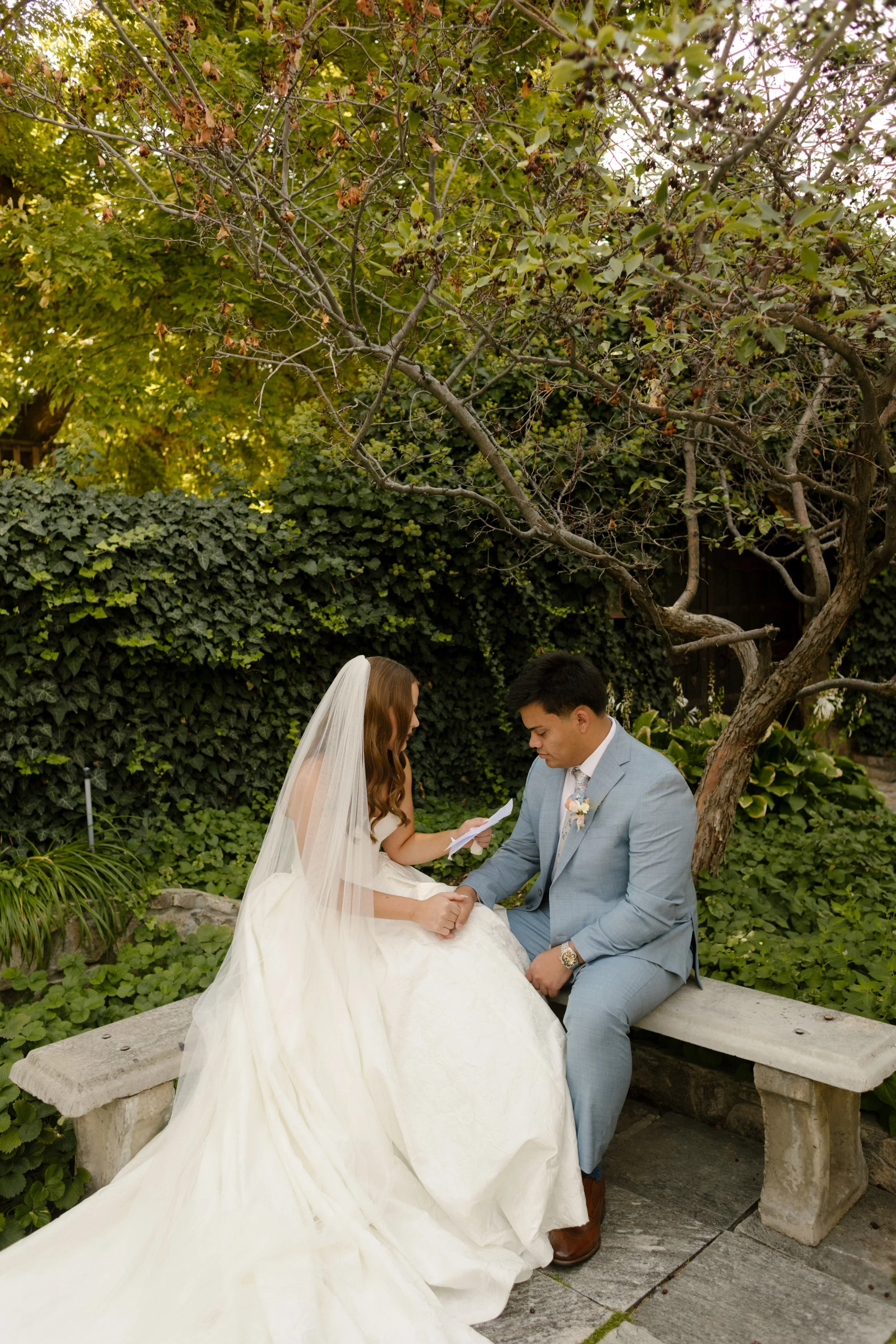 Bride and groom sitting on marble bench as bride reads her vows to her groom. 