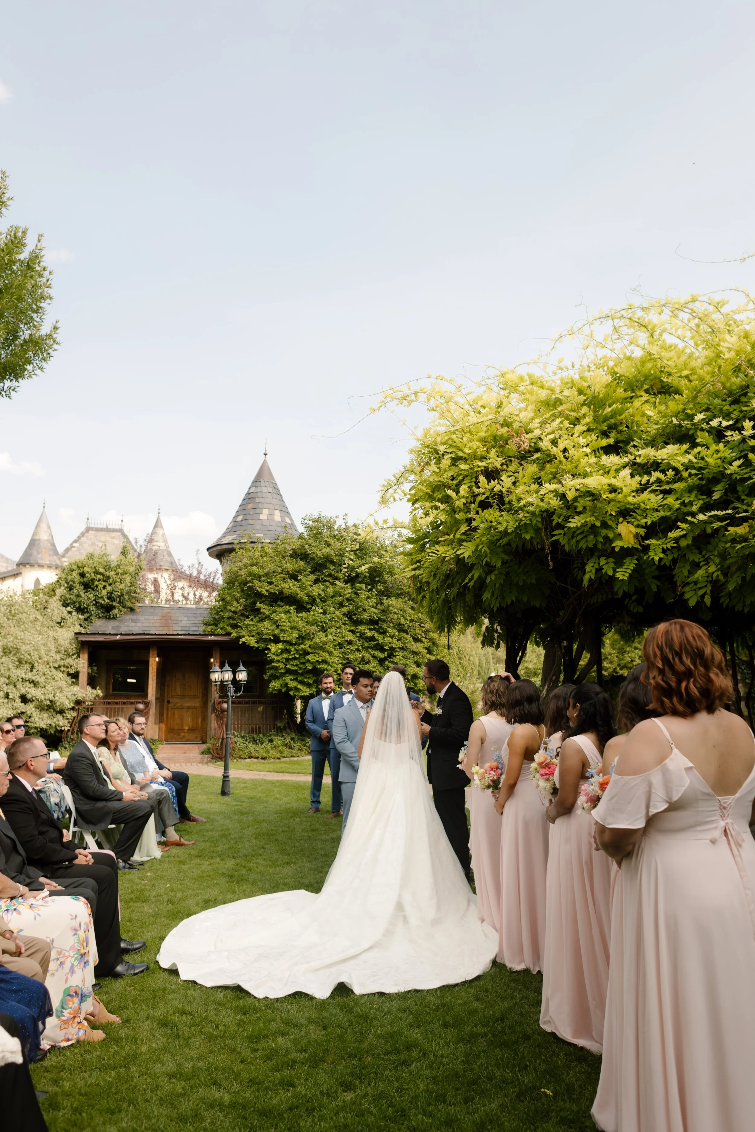 Wide view of outdoor ceremony with bride and groom at the altar, bridesmaids in blush dresses lined beside them at a beautiful utah wedding venue.