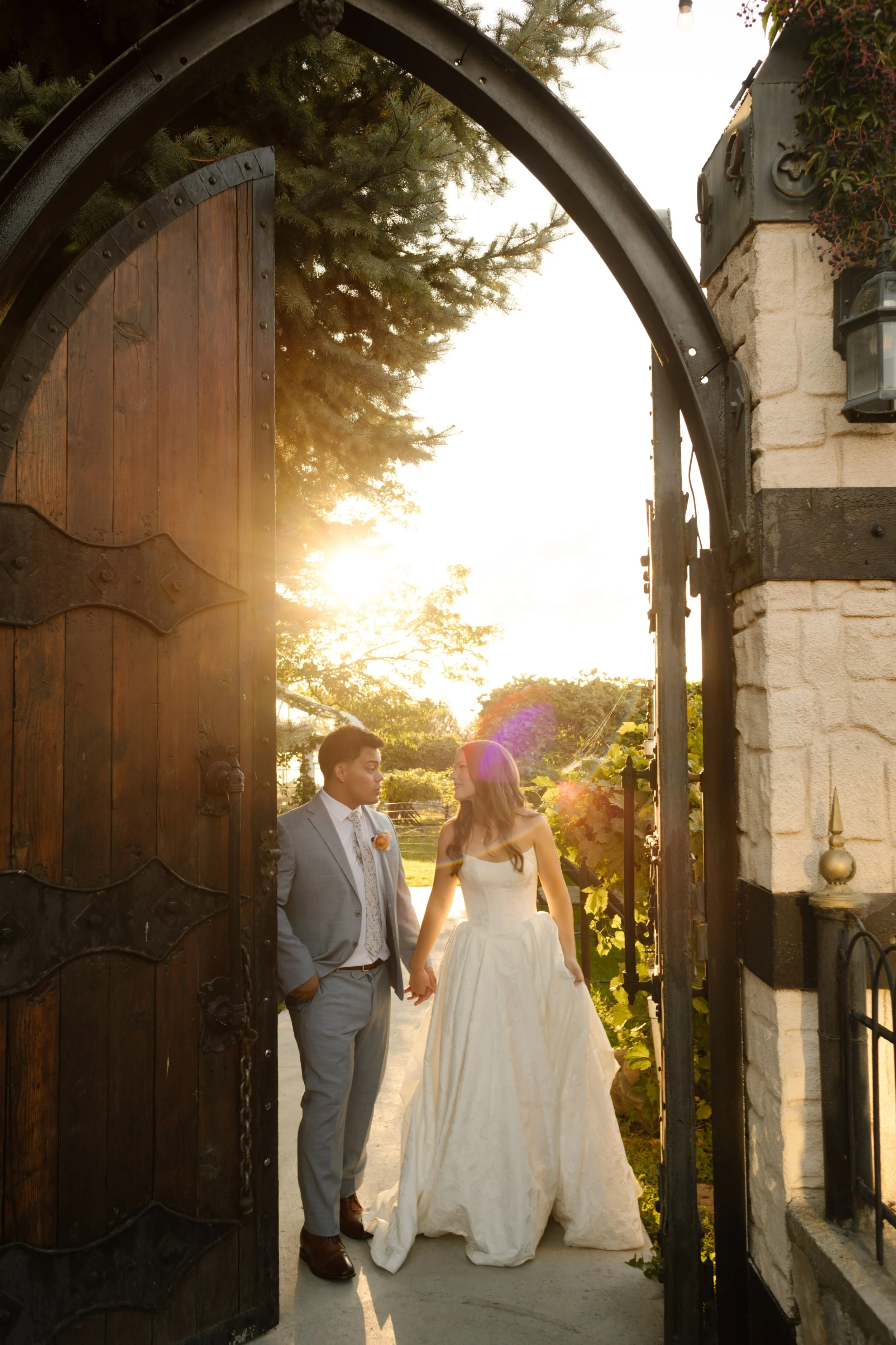 Bride and groom standing in a stone archway doorway with warm sunset light streaming through at a charming utah wedding venue.