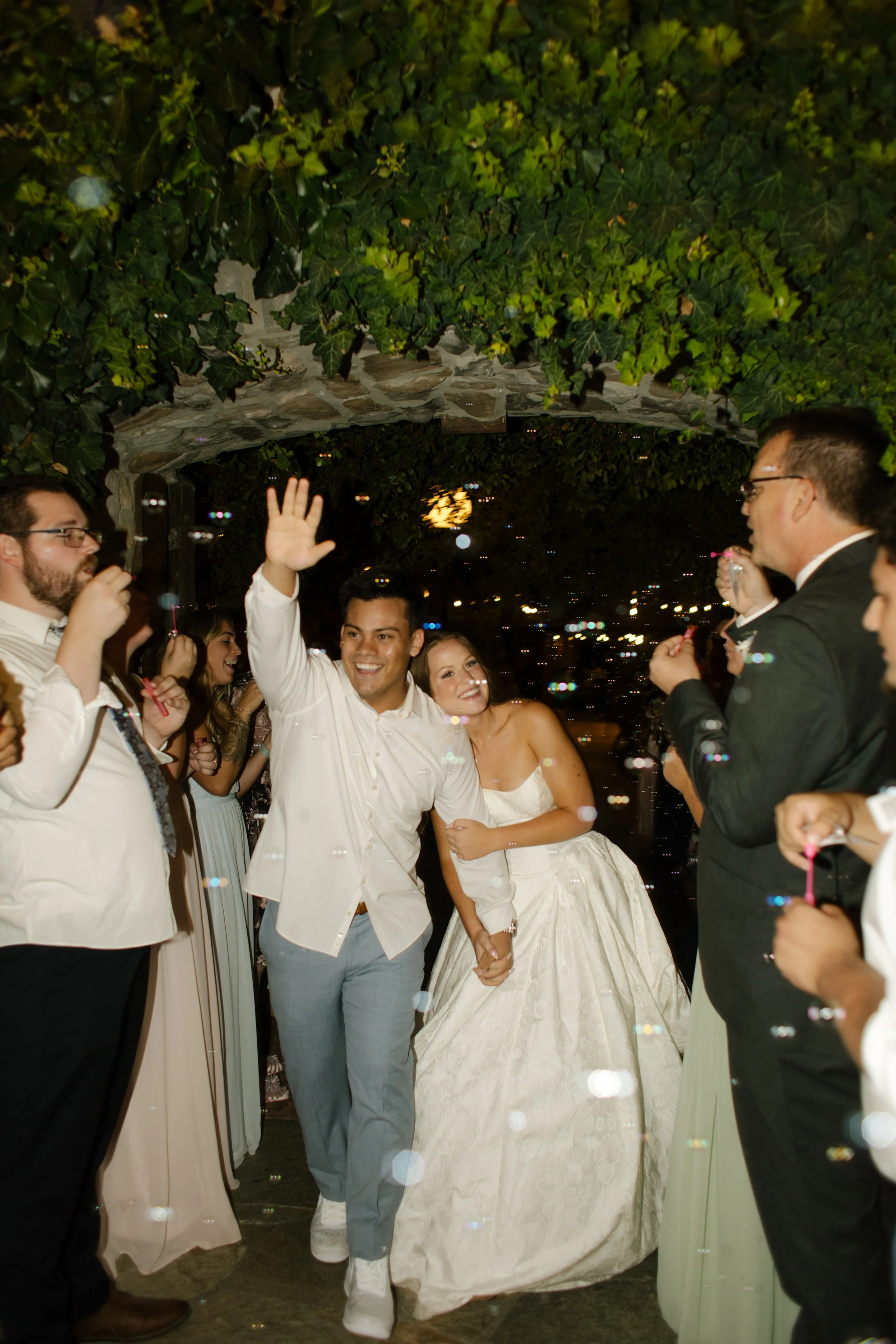 Bride and groom exit their wedding reception as newly married husband and wife as guests blow bubbles to celebrate. 