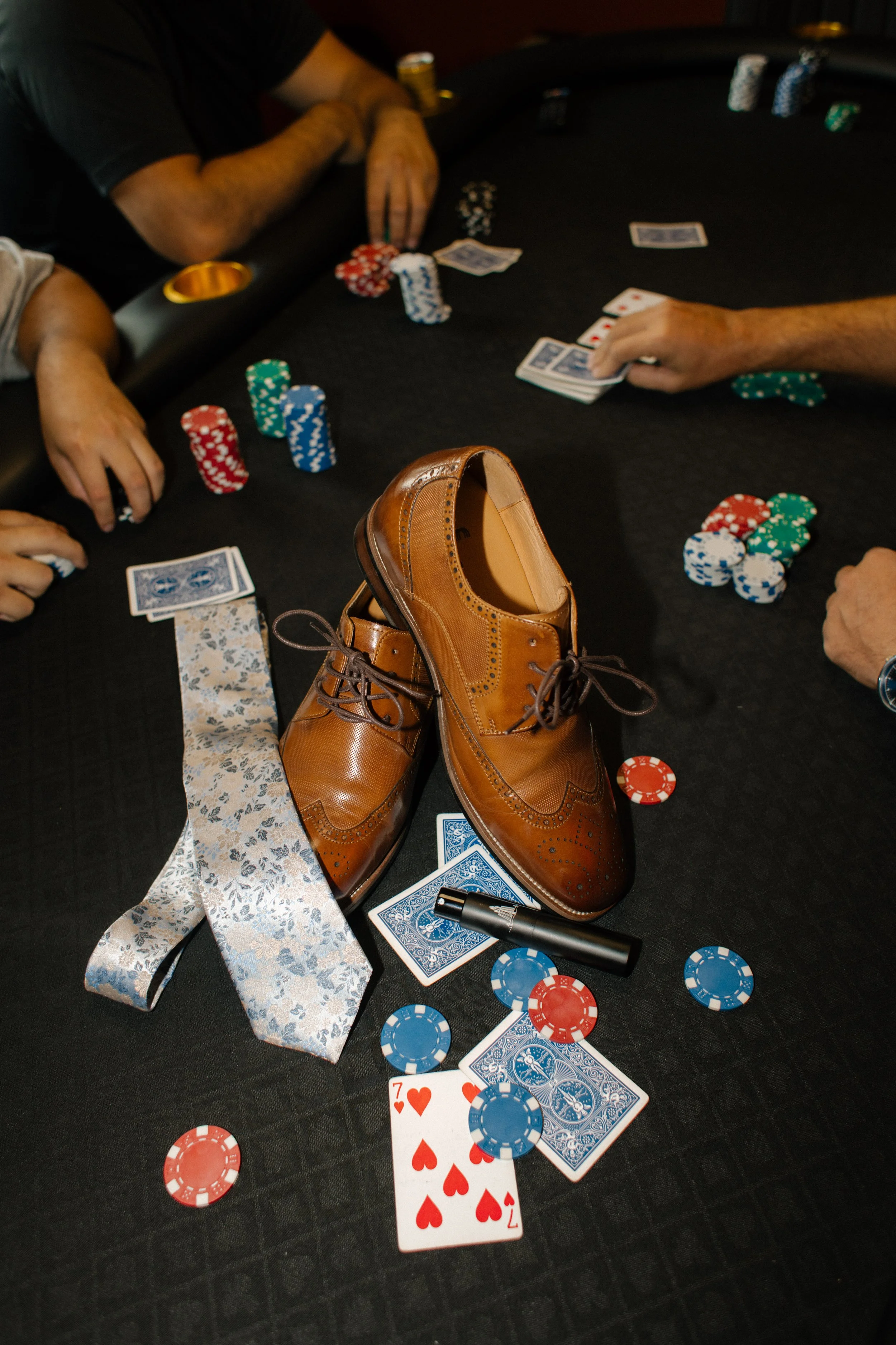 Groom's dress shoes sitting on poker table with poker chips and other groom's accessories around it. 
