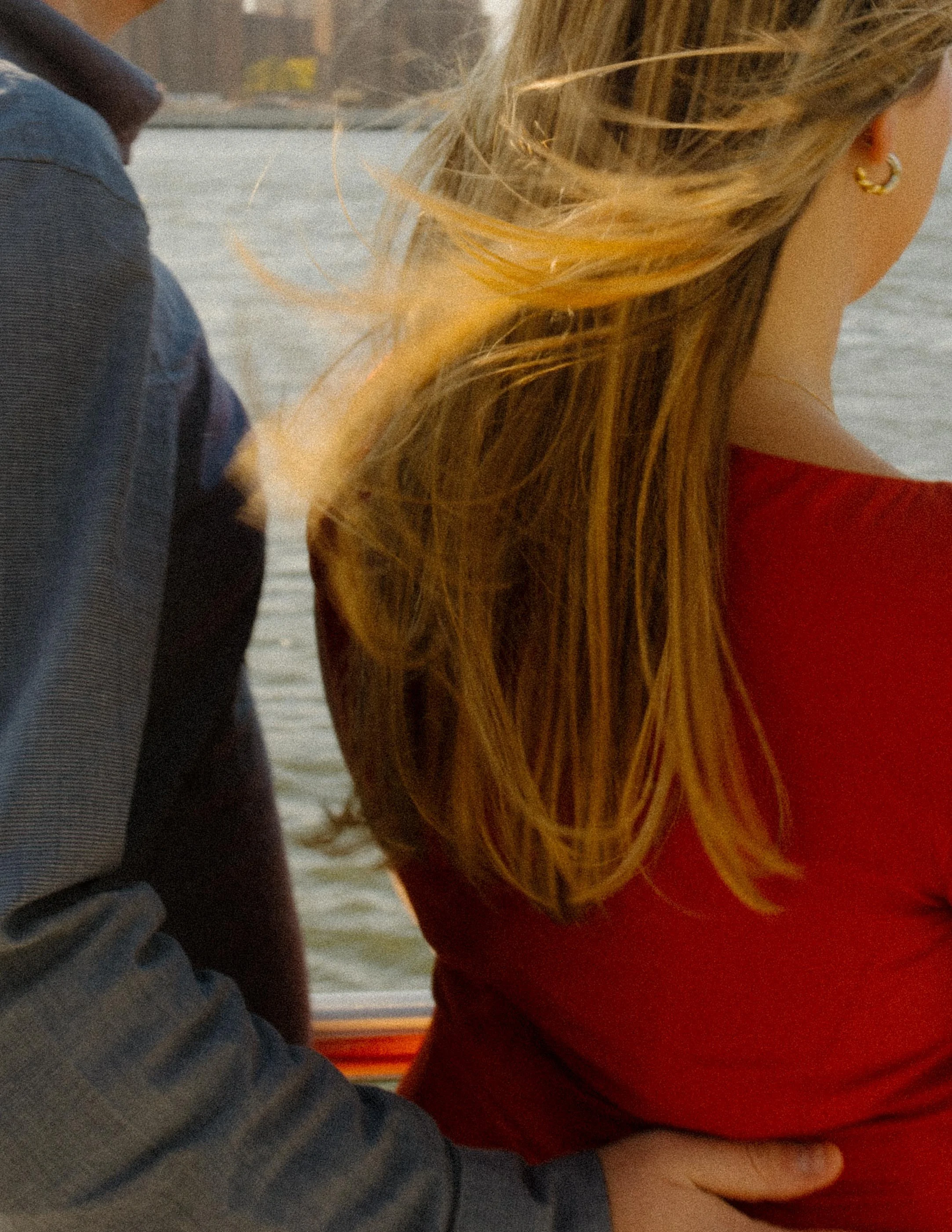Wind-swept close-up during nyc engagement photos along the East River, her red dress catching golden light.