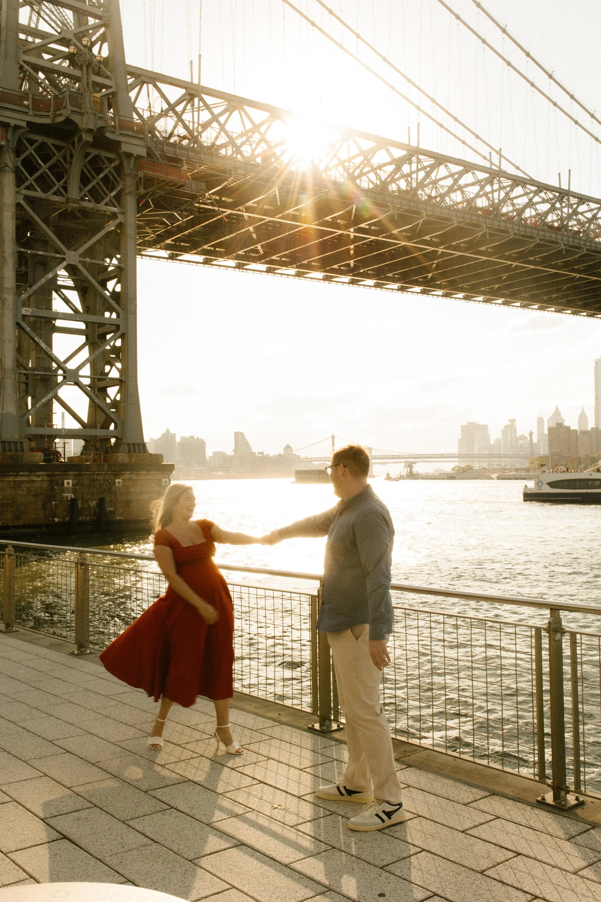 Golden hour nyc engagement photos beneath the Manhattan Bridge, bride-to-be twirling by the waterfront.