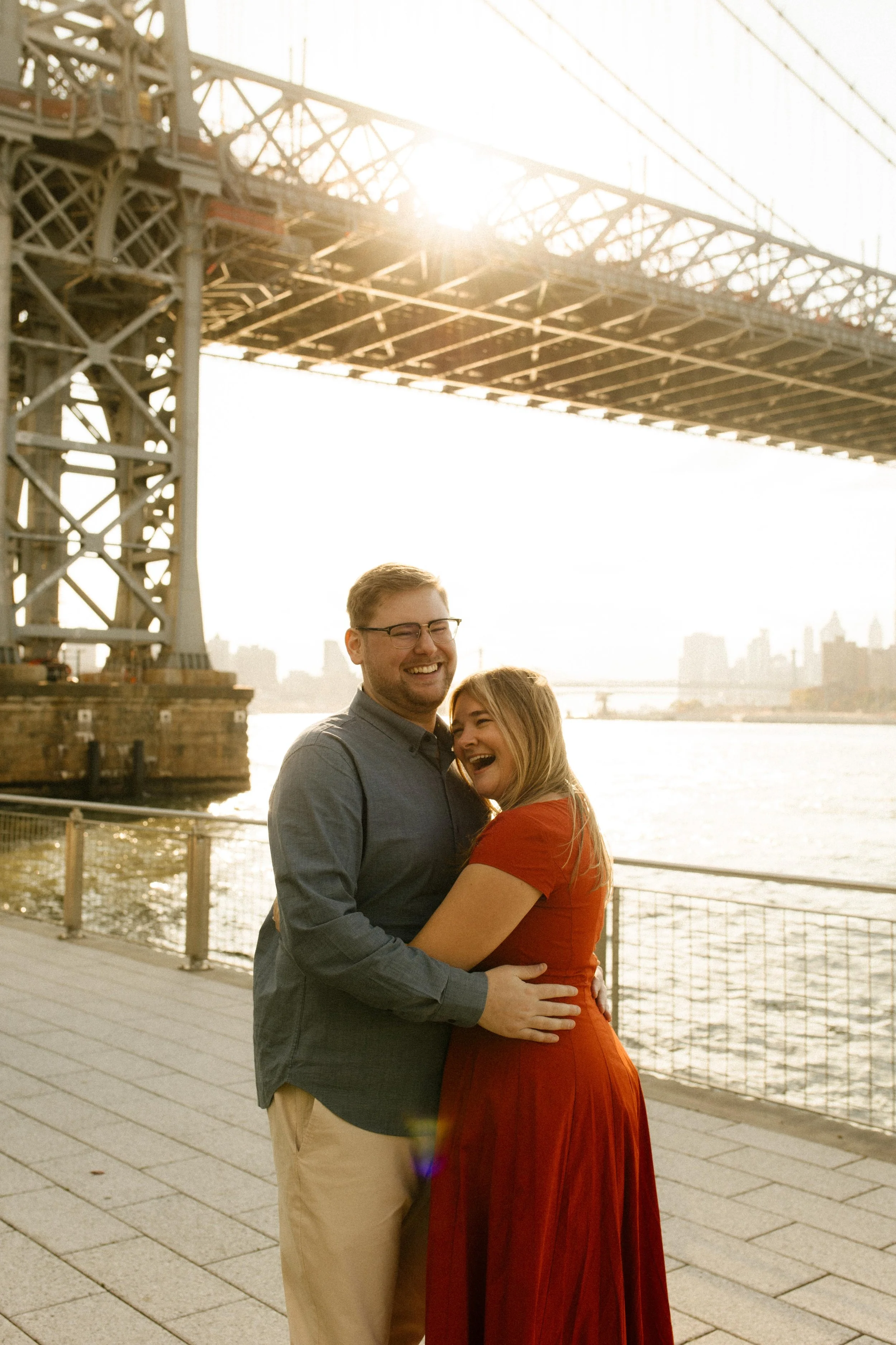 Joyful nyc engagement photos under the Manhattan Bridge at golden hour, couple laughing by the East River.