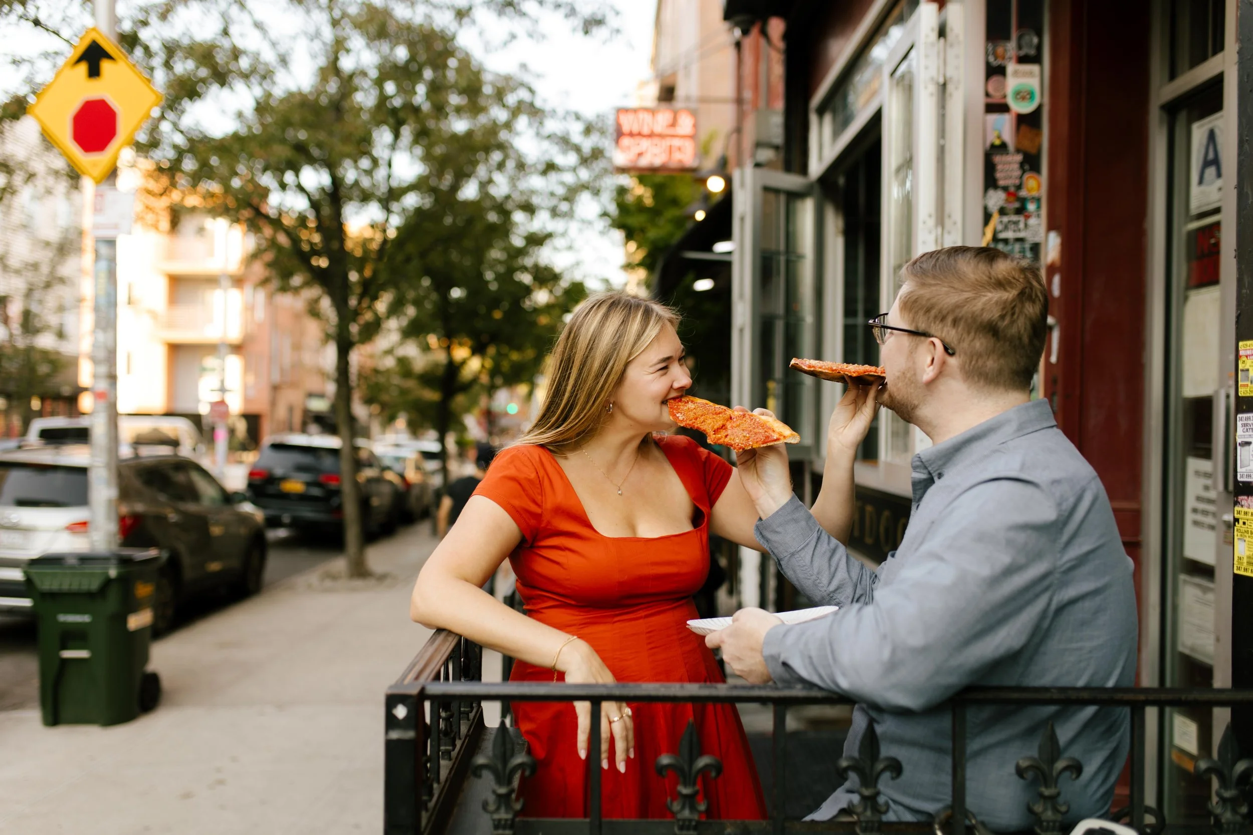 Playful nyc engagement photos of couple sharing oversized pizza slices outside a Brooklyn spot.