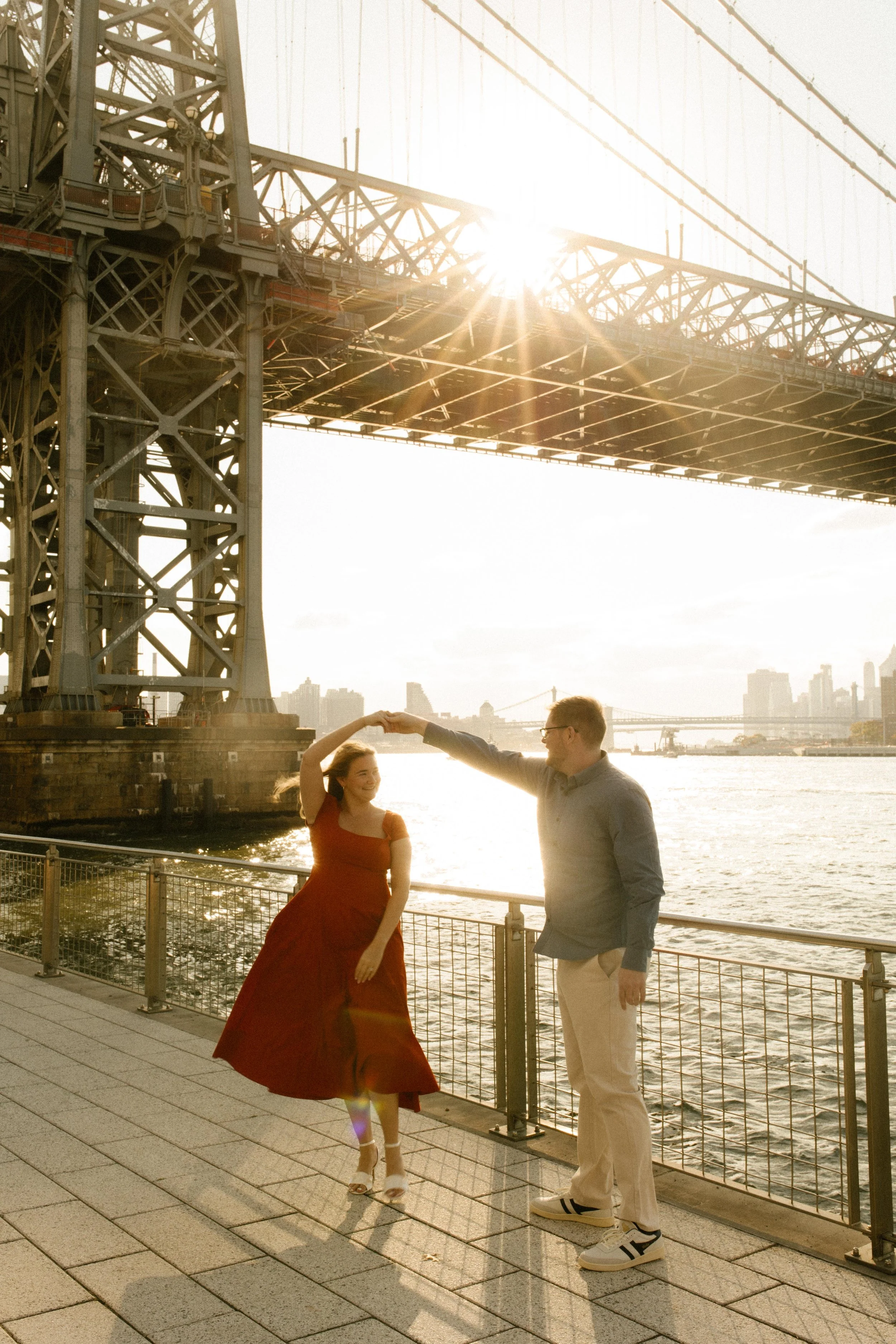 Playful nyc engagement photos of bride-to-be twirling in red dress under the Manhattan Bridge.