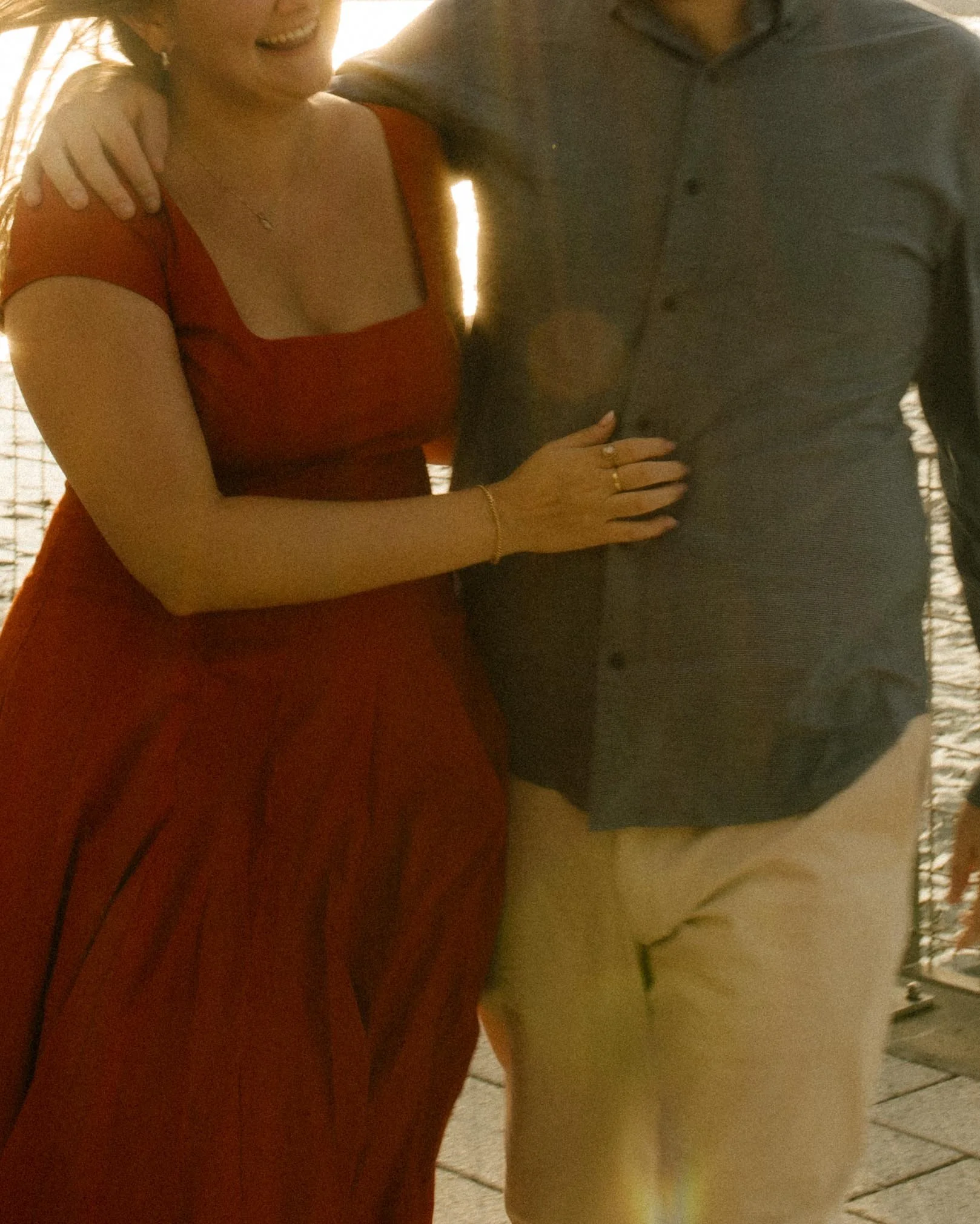 Detail photo of bride-to-be’s red dress and engagement ring during golden hour waterfront session.