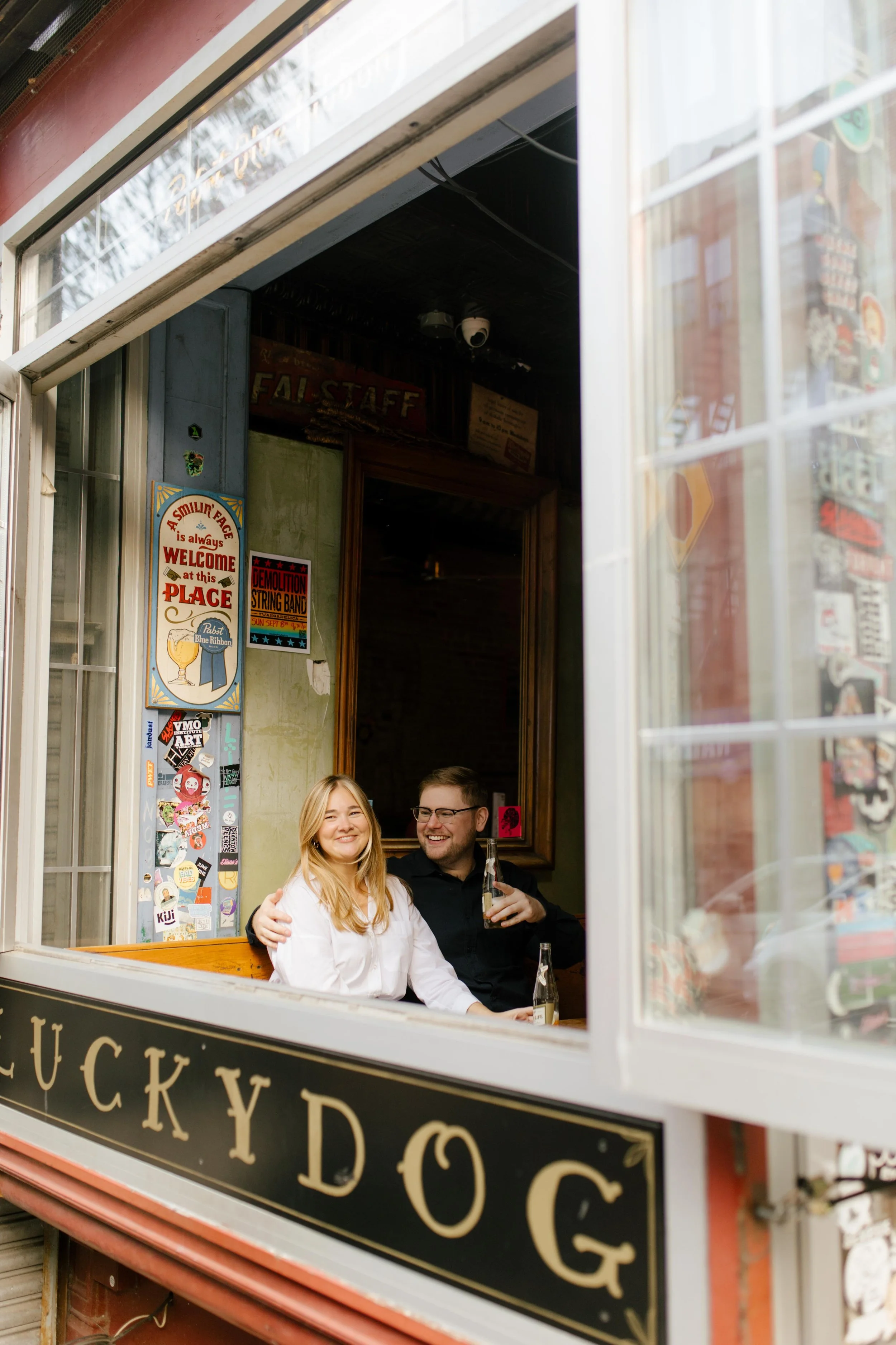 Candid nyc engagement photos of couple sitting inside a Brooklyn bar framed by an open window.