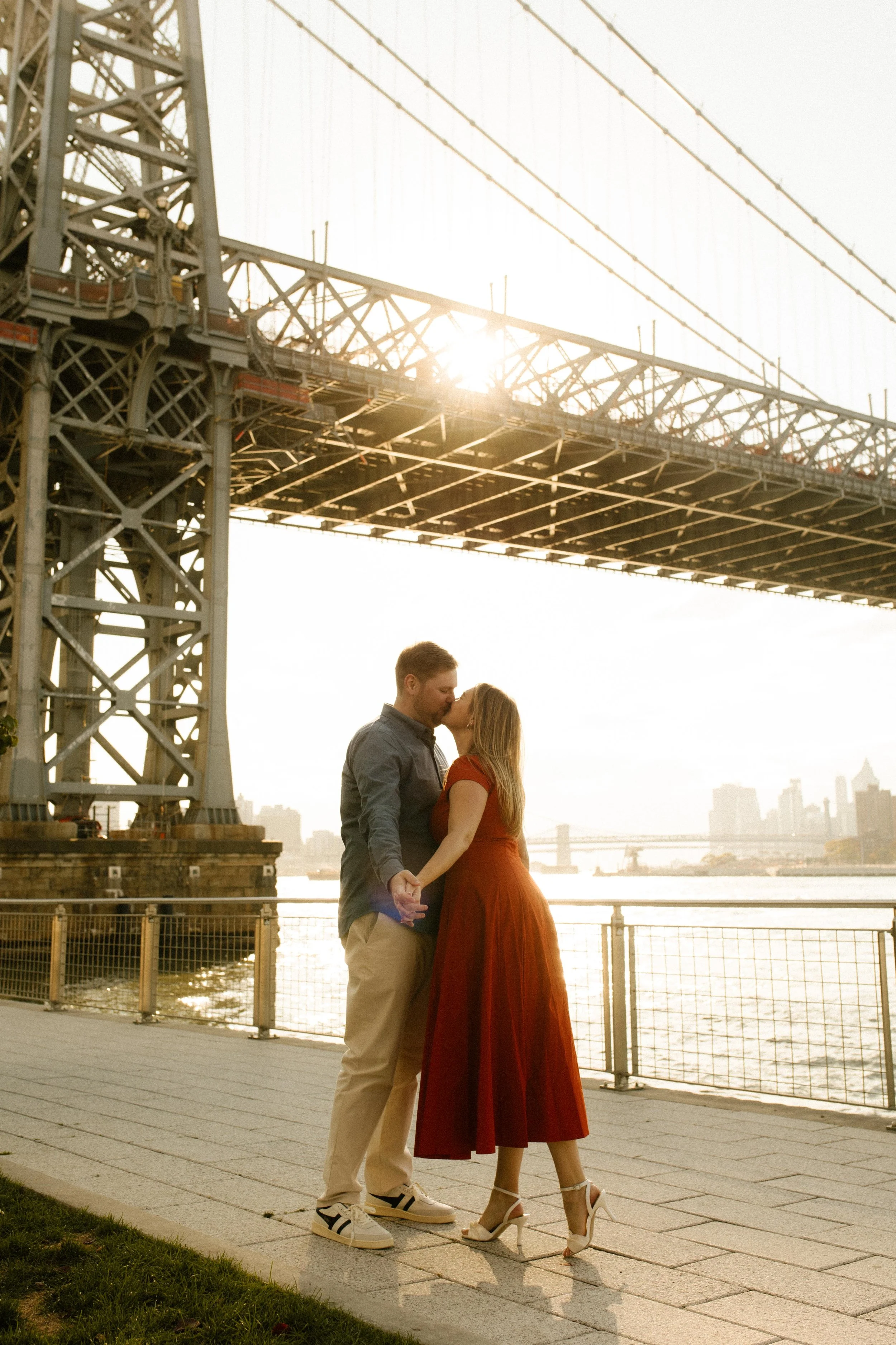 Golden hour kiss during nyc engagement photos on the Brooklyn waterfront beneath the Manhattan Bridge.