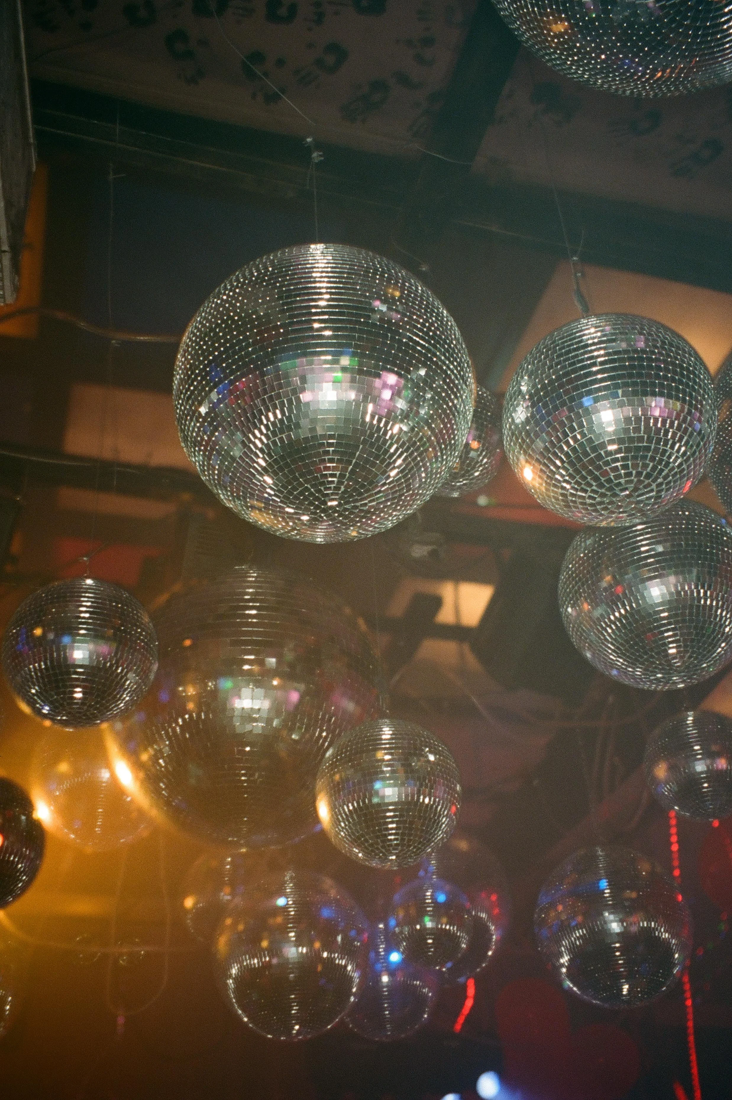 A ceiling filled with mirrored disco balls reflects warm amber and colorful lights, setting the nostalgic nightclub mood for unforgettable wedding after parties.