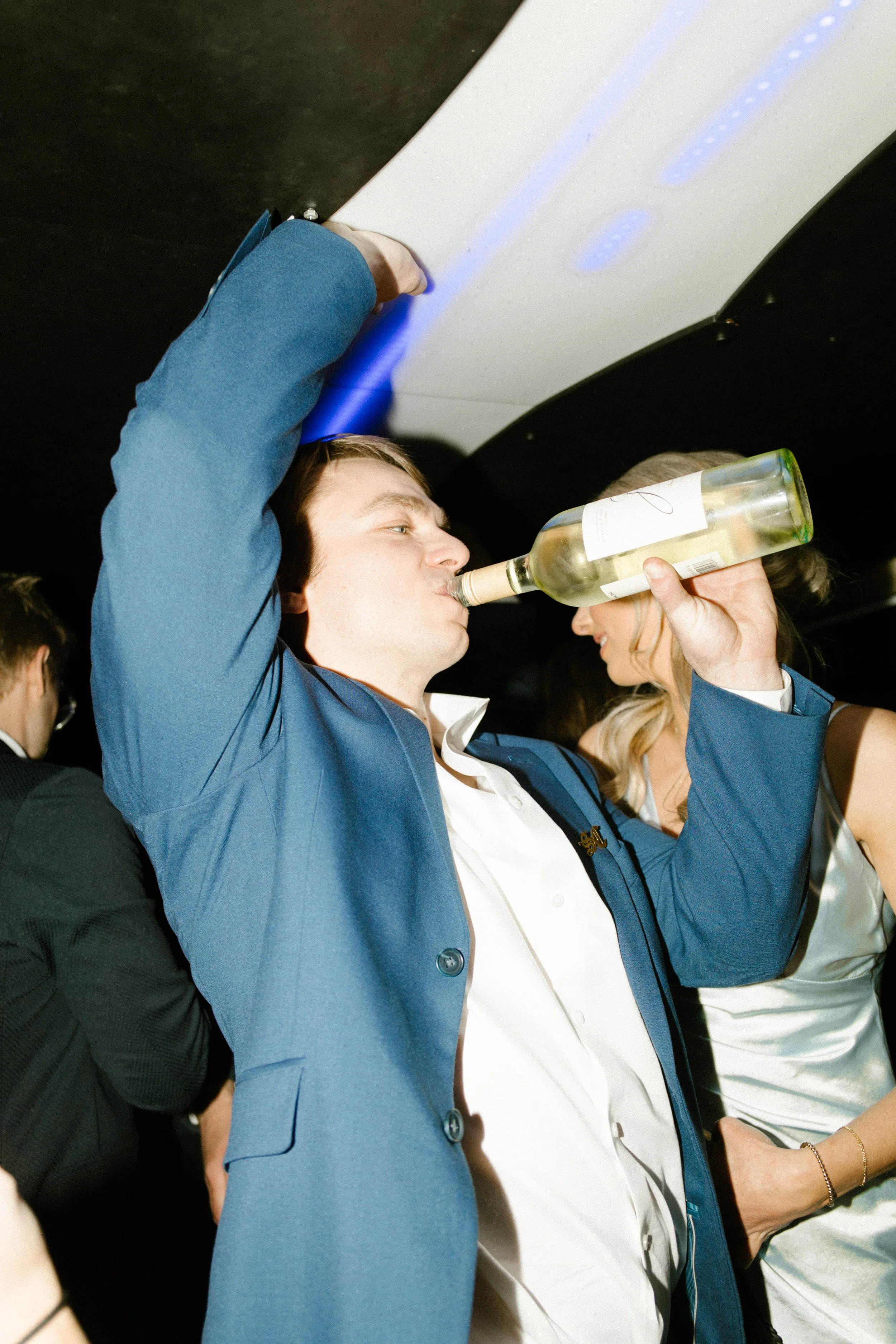 Wedding guest drinking straight from a wine bottle while dancing on a packed dance floor during wedding after parties.