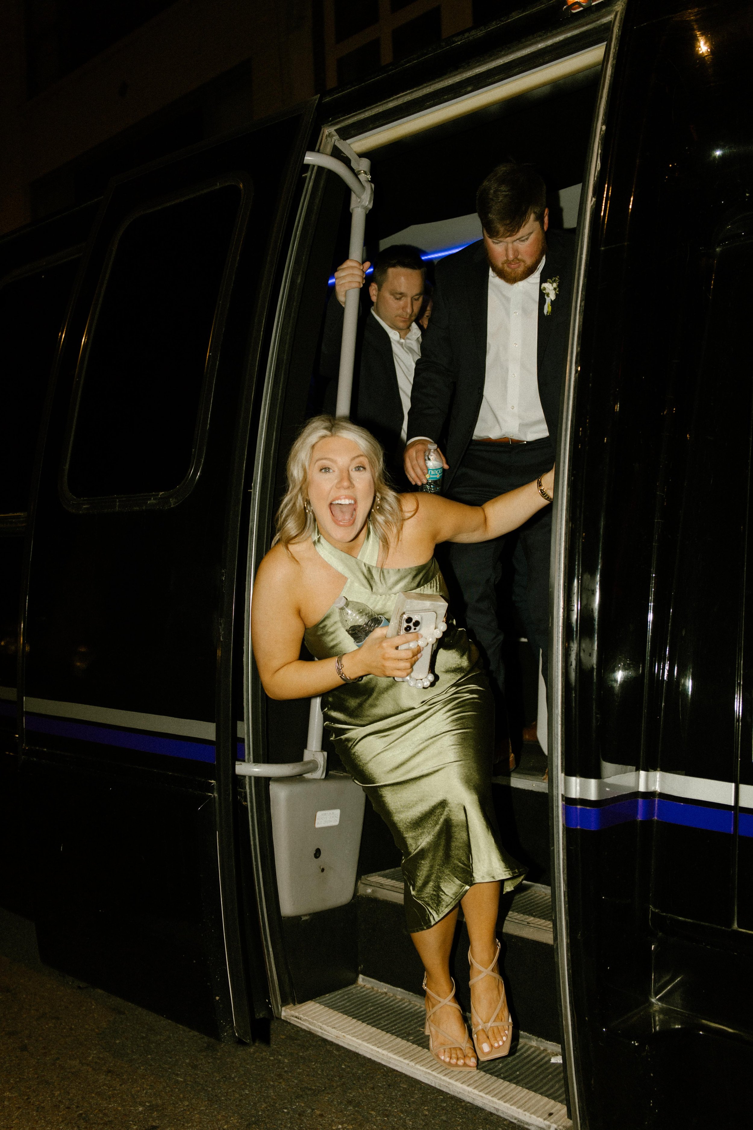 Bridesmaid excitedly stepping out of a party bus with friends arriving for wedding after parties.